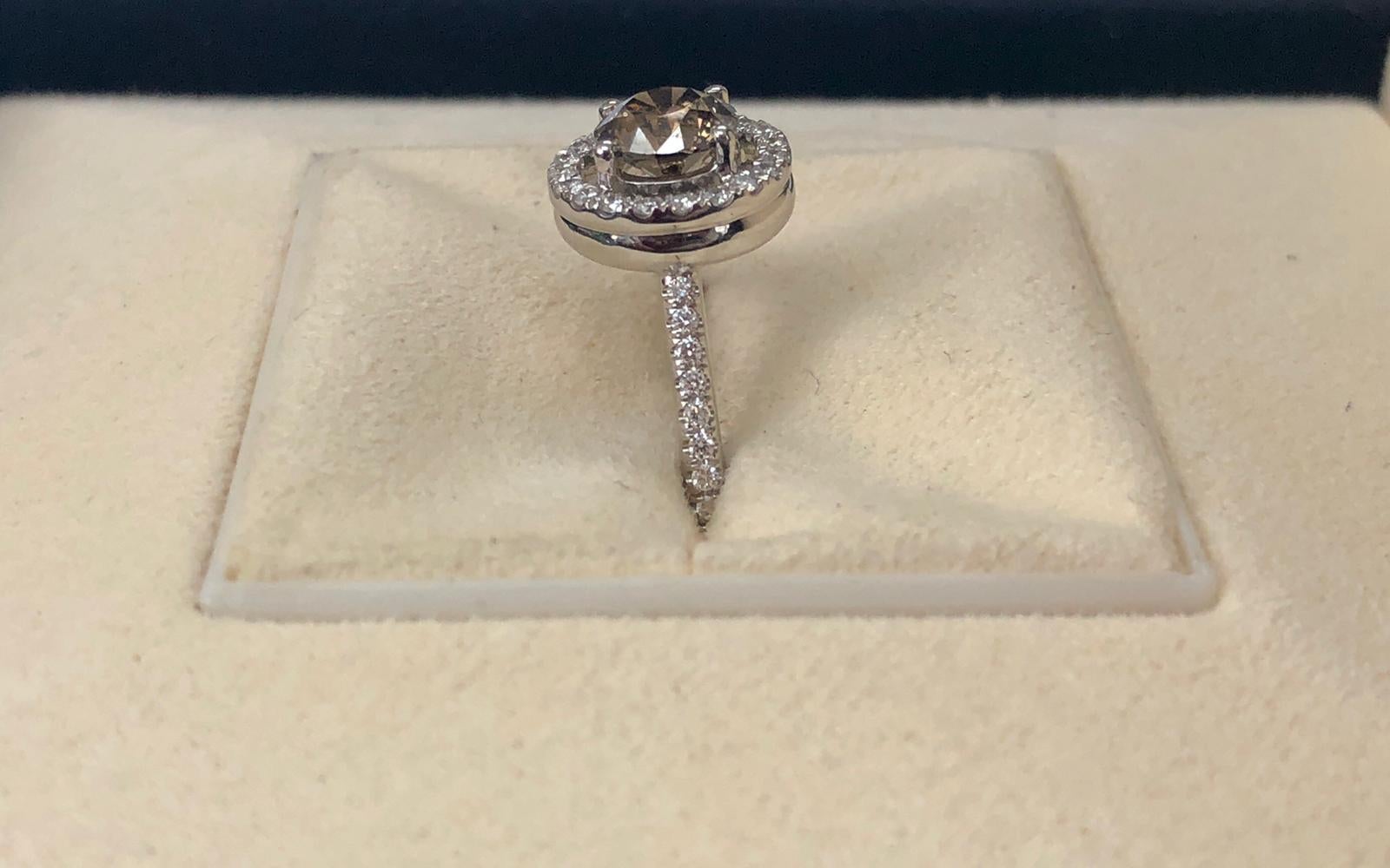 Fancy dark yellowish brown natural round diamond weighing 1.05 carats by GIA.  Half way paved white diamonds in the halo setting. Its transparency and luster are excellent. set on 18K white gold, this ring is the ultimate gift for anniversaries,