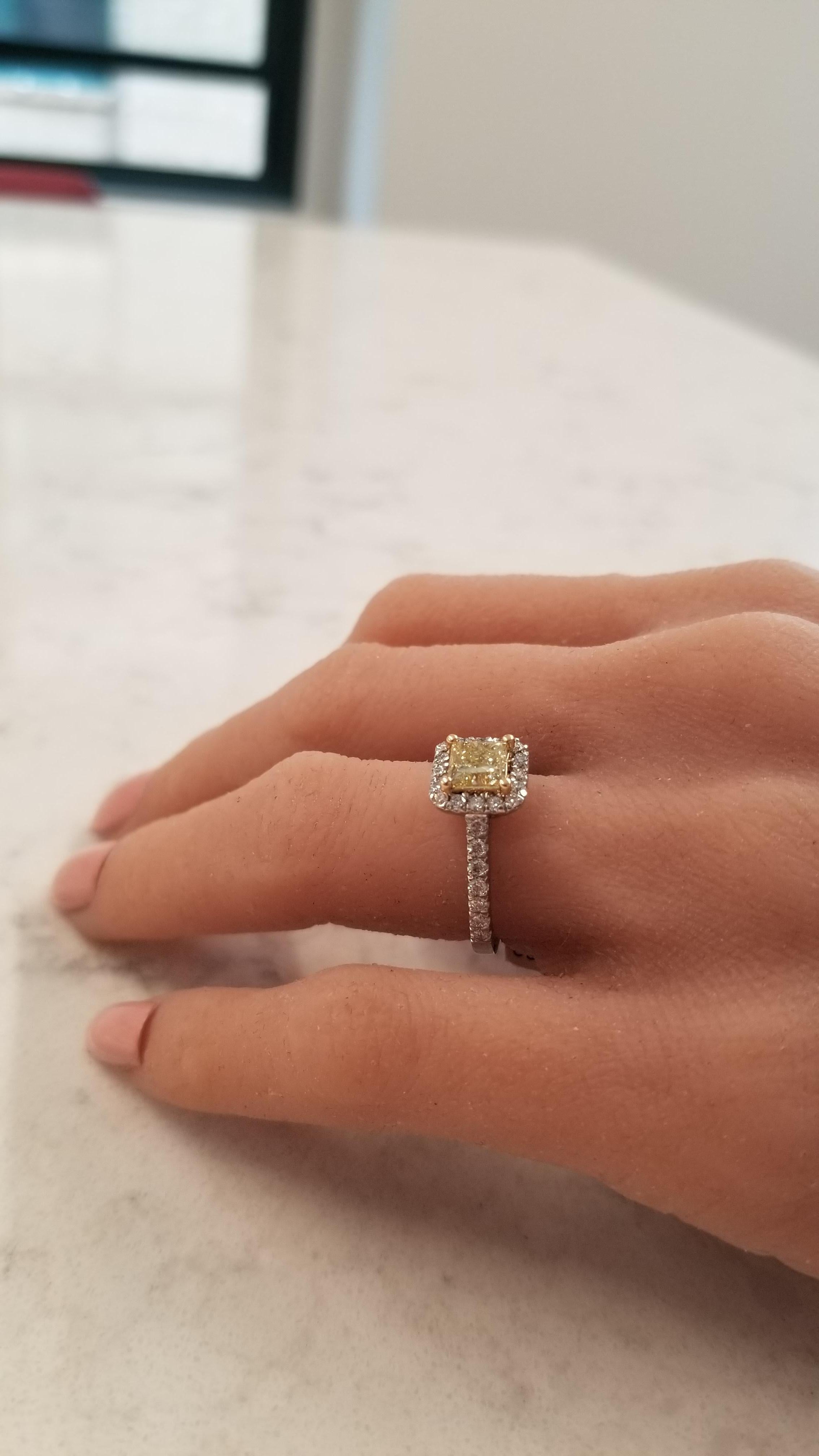 This is a GIA certified 1.06 carat princess cut, natural fancy yellow diamond measuring 5.34x5.30x4.14mm. This natural yellow diamond is framed by scintillating round brilliant cut white diamonds prong set in a halo cluster and down the sides of the