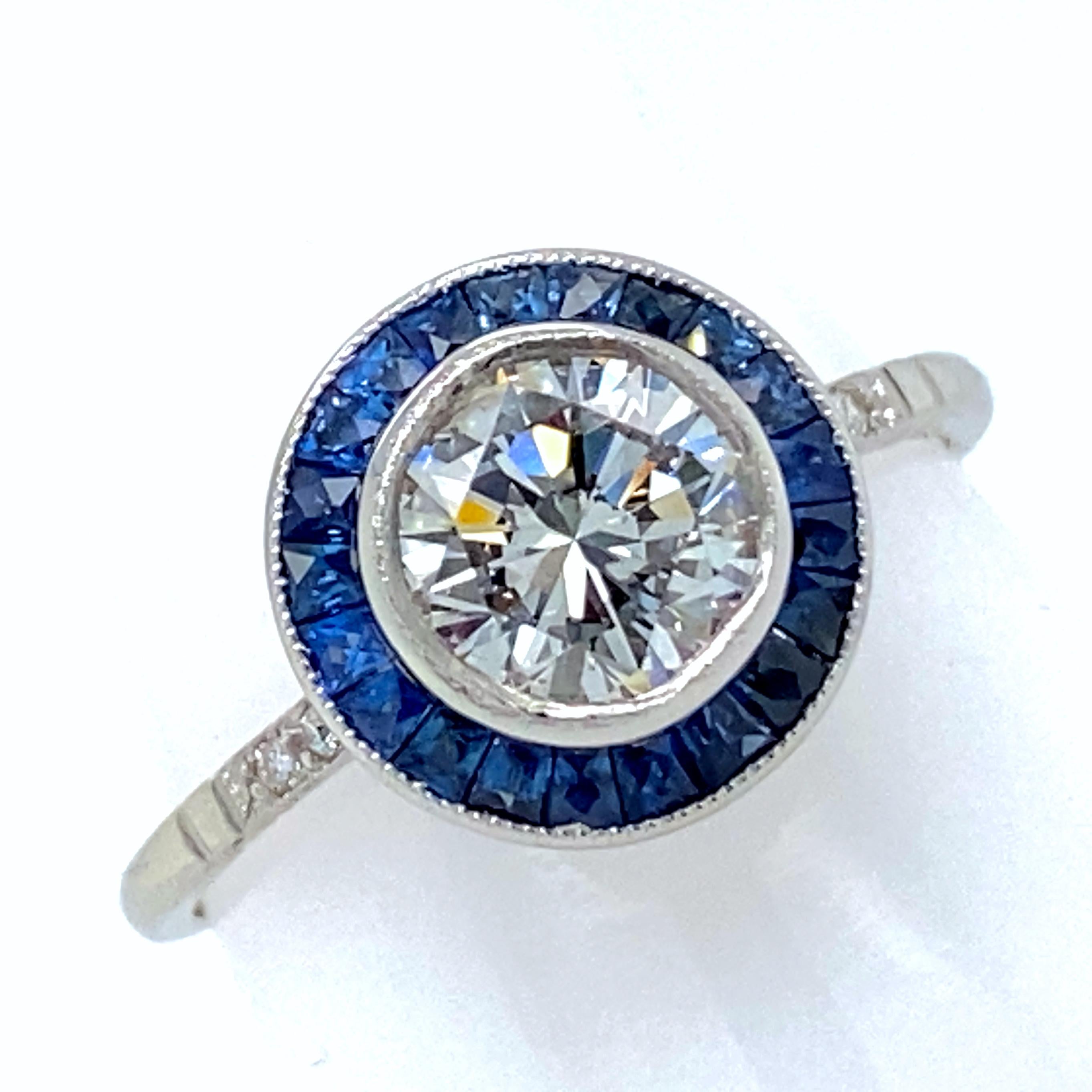 This faithful reproduction of a classic Art Deco design features a channel-set round halo of natural sapphires around a certified diamond plus pavé-set diamond shoulders.  

The center diamond is a 1.19 carat brilliant cut round, and it's an