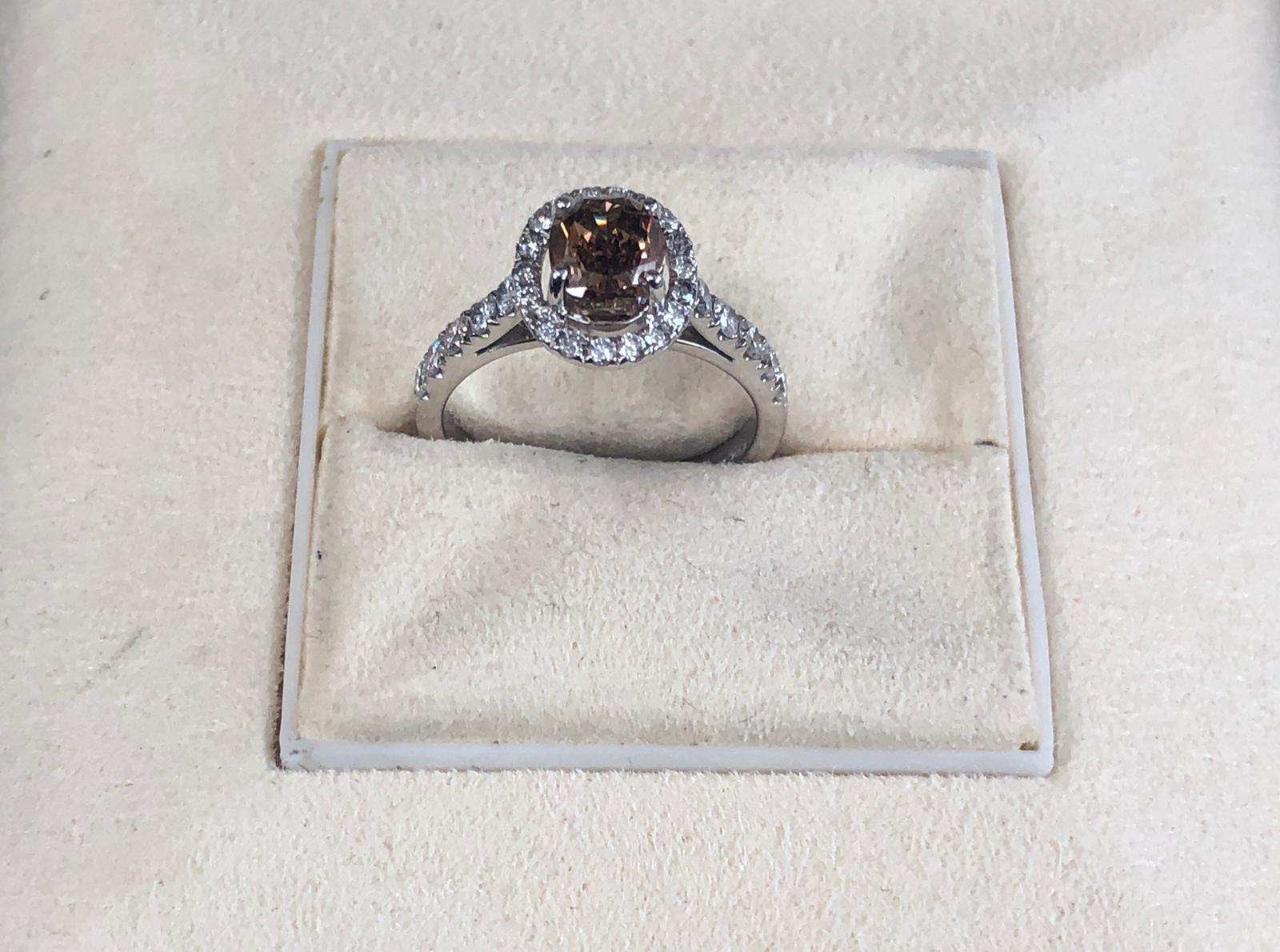 Natural Fancy Dark Orangy Brown Oval Shape Diamond Weighing 1.19 carats by GIA.  Half way paved white diamonds in the halo setting. Its transparency and luster are excellent. set on 18K white gold, this ring is the ultimate gift for anniversaries,