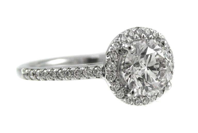 Set within a luxurious platinum hand crafted mounting with round brilliant cut diamonds cascading down each side of the platinum shank, the center halo of bright white and sparkly diamonds showcases a wonderful, beautifully cut round brilliant cut