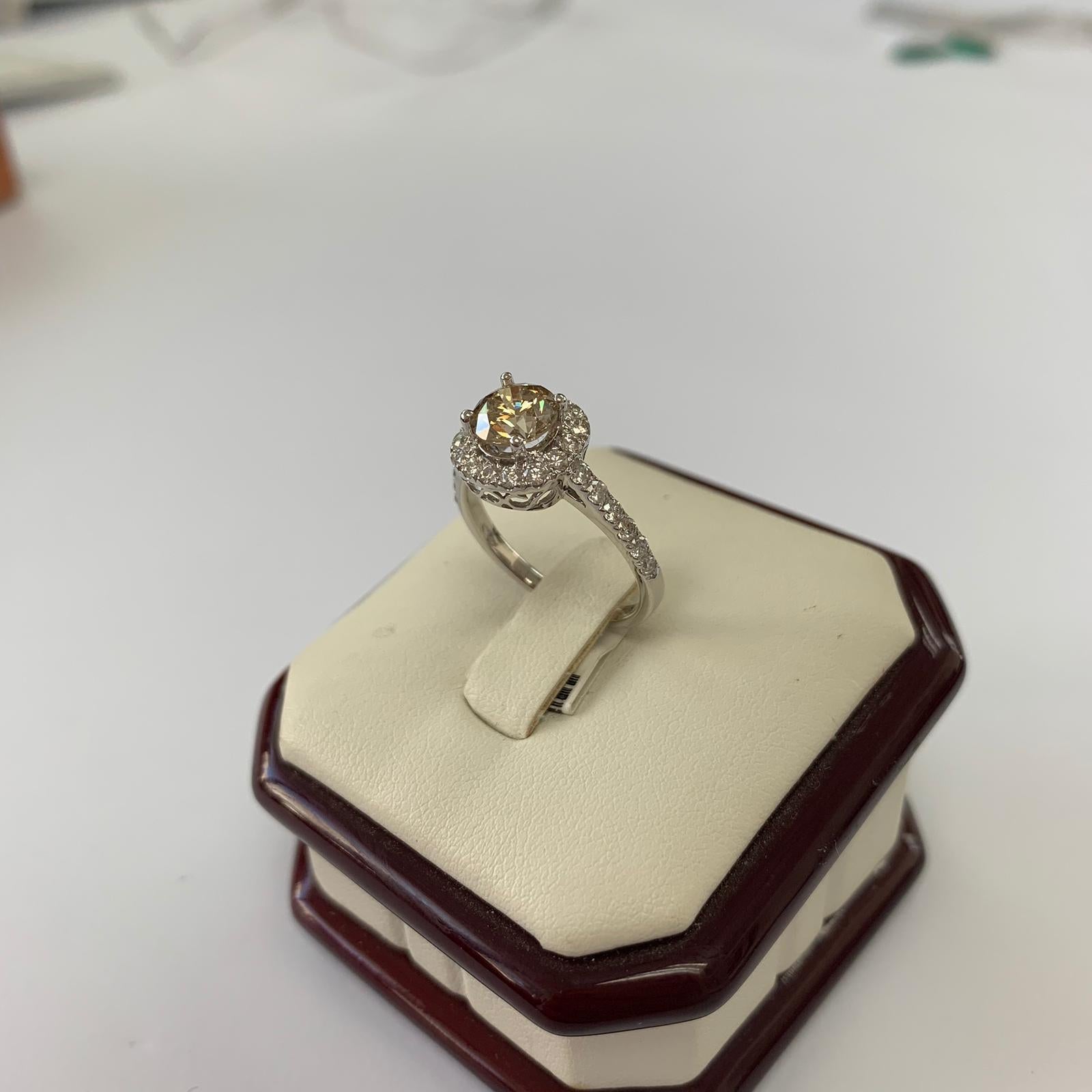 Fancy light yellowish brown natural round diamond weighing 1.28 carats.  Half way paved white diamonds in the halo setting. Its transparency and luster are excellent. set on 18K white gold, this ring is the ultimate gift for anniversaries,