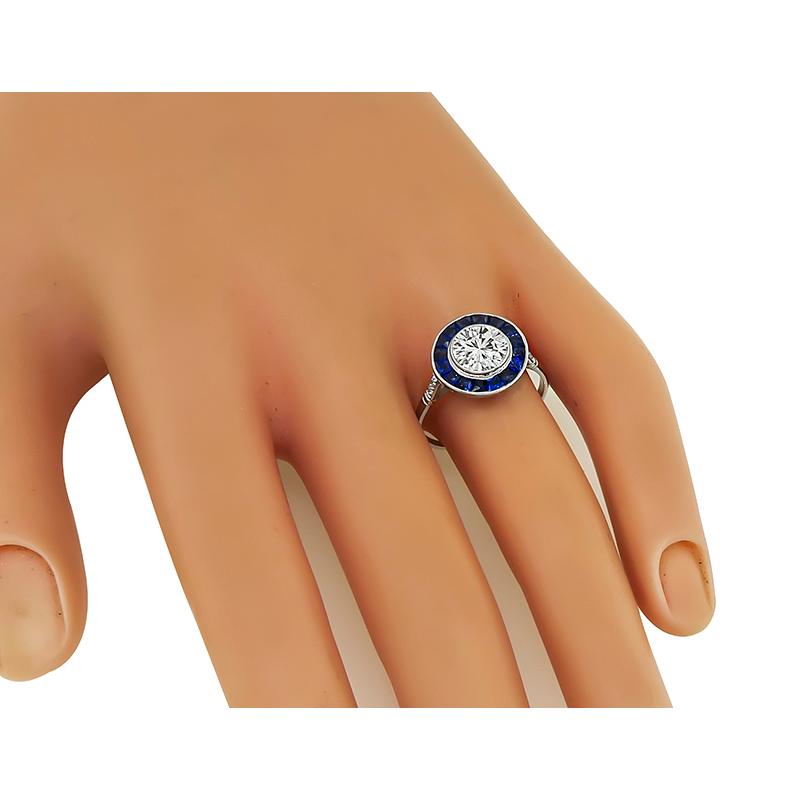This is an elegant 18k white gold halo engagement ring. The ring is centered with a sparkling GIA certified round cut diamond that weighs 1.29ct. The color of the diamond is L with VS1 clarity. The center diamond is accentuated by lovely sapphire