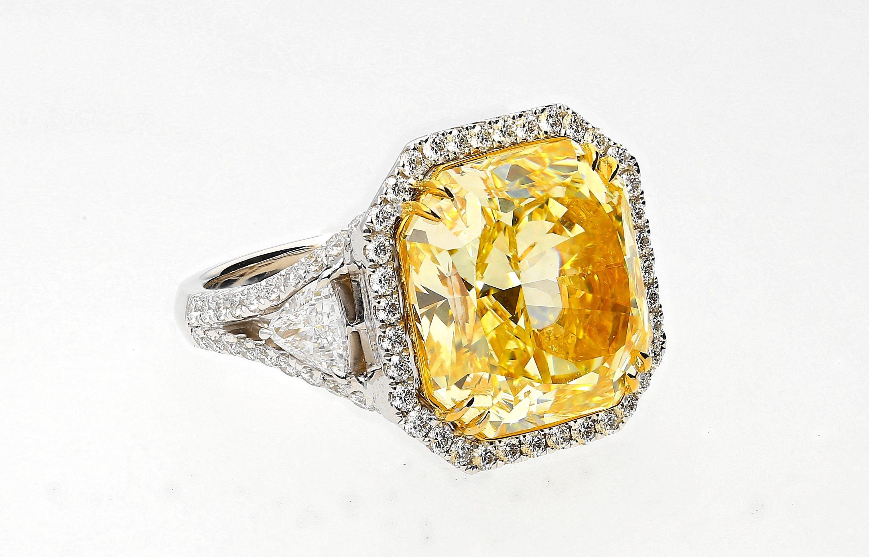 Centering a magnificent 13.14 Carat Radiant-Cut Fancy Intense Yellow Colored Diamond of VVS1 Clarity, accented by an additional nearly 2 carats of White Diamonds, and set in lavish 18K White Gold, this masterpiece is the quintessential