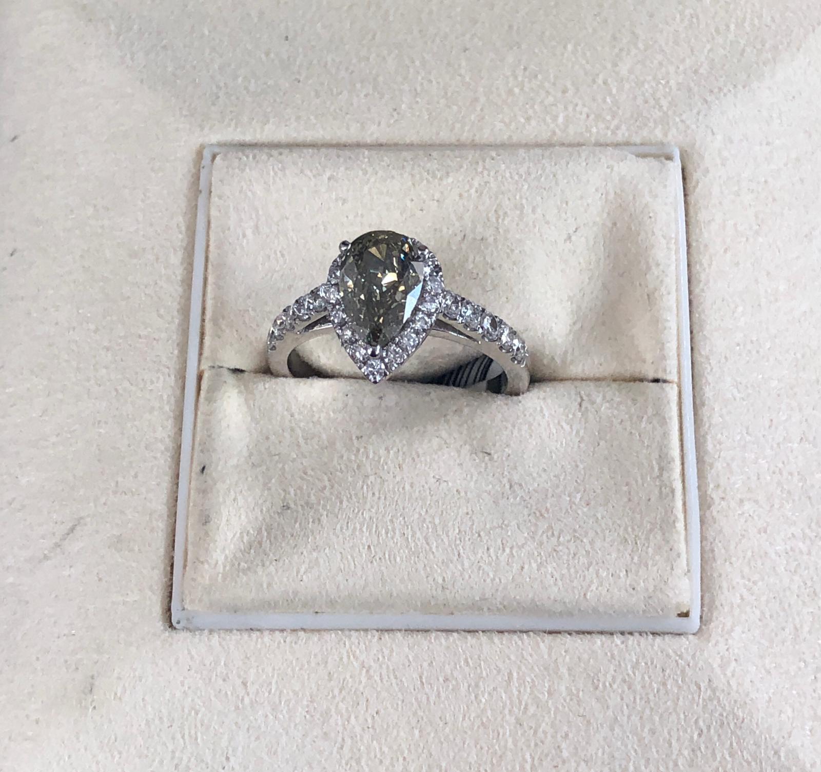 Natural Fancy Dark Gray-Greenish Yellow Pear shape diamond weighing 1.35 carats by GIA.  Half way paved white diamonds in the halo setting. Its transparency and luster are excellent. set on 18K white gold, this ring is the ultimate gift for