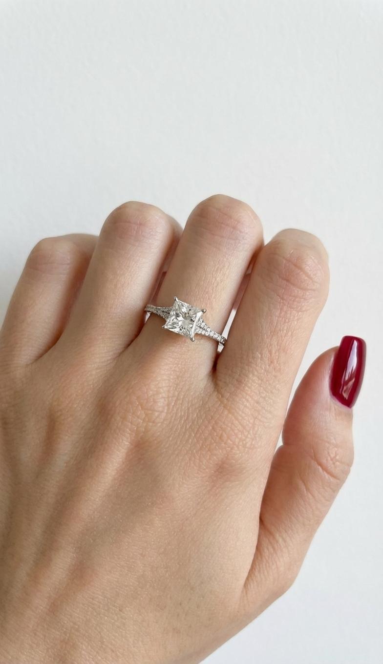 Questo squisito anello di fidanzamento di A. Simon è caratterizzato da un diamante centrale mozzafiato da 1,20 carati con taglio a principessa, certificato GIA e montato con eleganza in un lussuoso oro bianco da 18 carati. Con altri diamanti