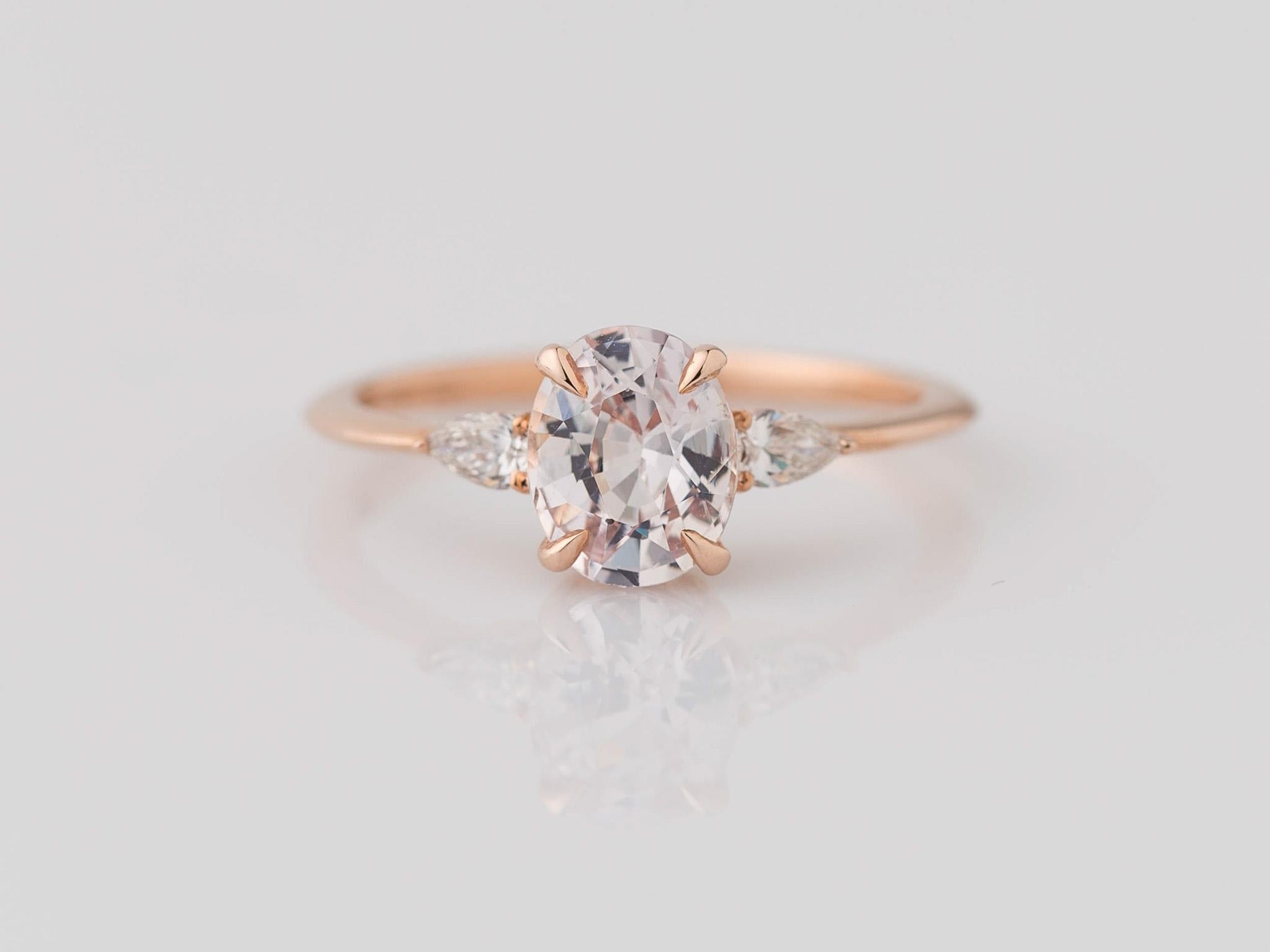 Indulge in the enchanting beauty of our GIA-certified 14K Rose Gold 3-Stone Oval Pink Sapphire Diamond Ring. At its heart lies a captivating oval-cut light pink sapphire, weighing 1.39 carats and measuring 7.45x5.95x4.12mm. Flanking this center