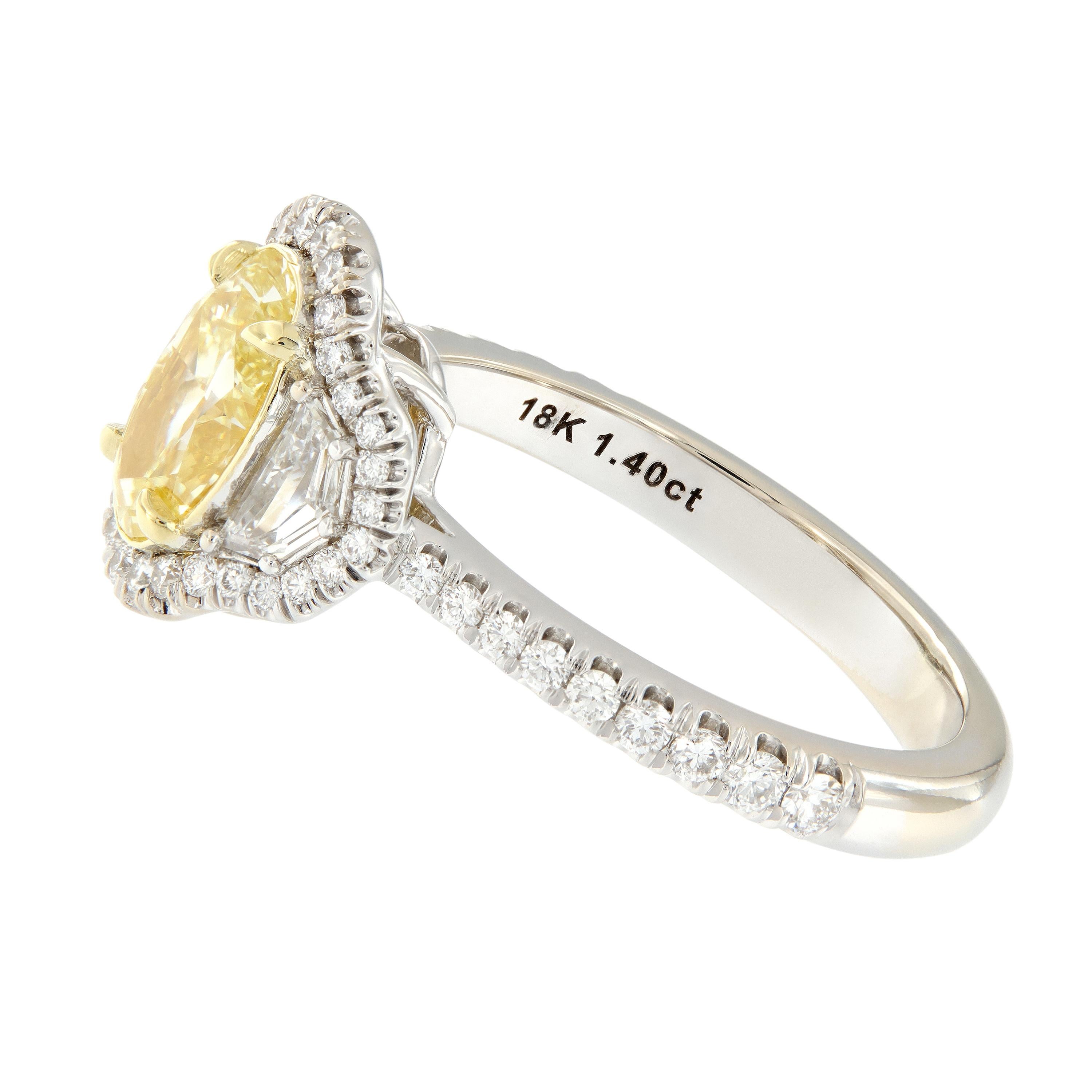 This pretty 18k white and yellow gold engagement ring features a stunning fancy yellow oval shaped diamond and is accented by Cadillac shaped step cut side diamonds. Pave set in a halo around the three center stones, in the side gallery and down the