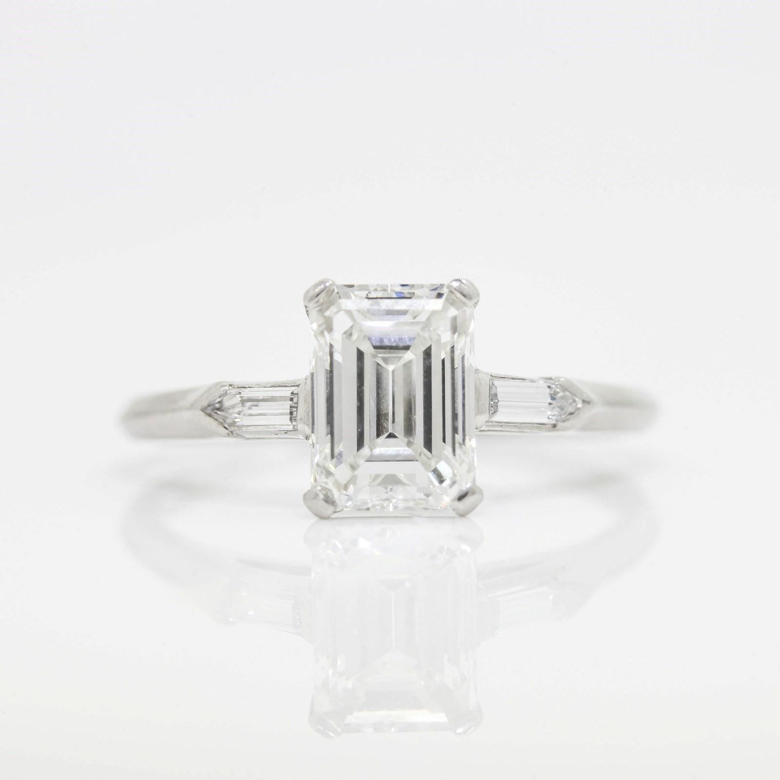 Classic vintage simplicity!   A platinum ring featuring a G.I.A. certified 1.44 carat Emerald Cut Diamond, accompanied by Report #5191830806 stating diamond is H color - VS1 clarity.  The four prong double wire basket setting is accented with two
