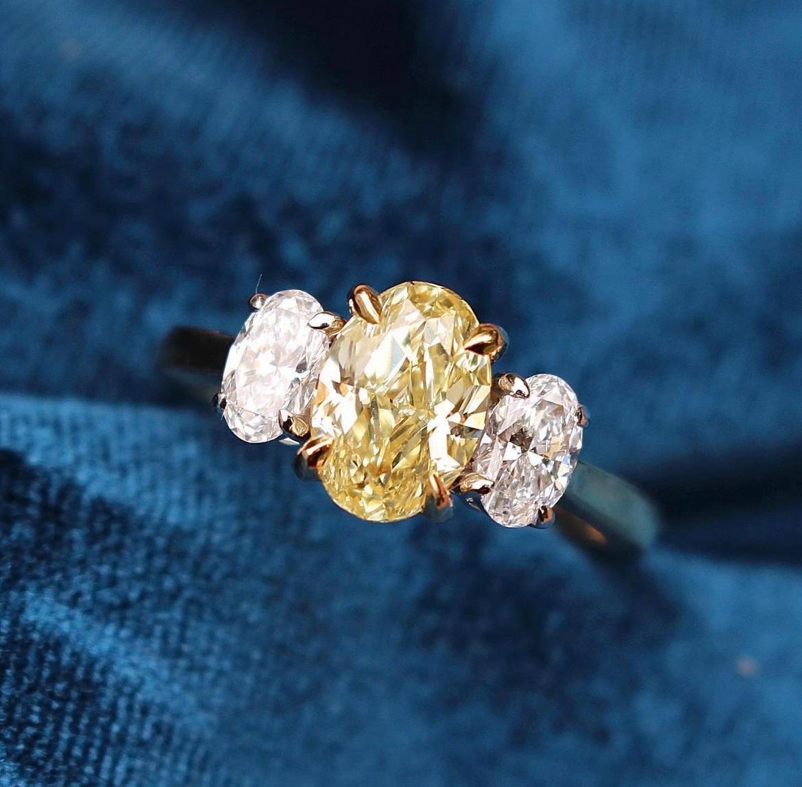 Centered upon a 1.5 Carat Oval shaped Yellow Diamond. Flanked by Oval diamonds weighing 0.60 Carats. 

Center stone is certified Fancy Yellow by GIA. 

Set in Platinum and 18 Karat Yellow Gold. 