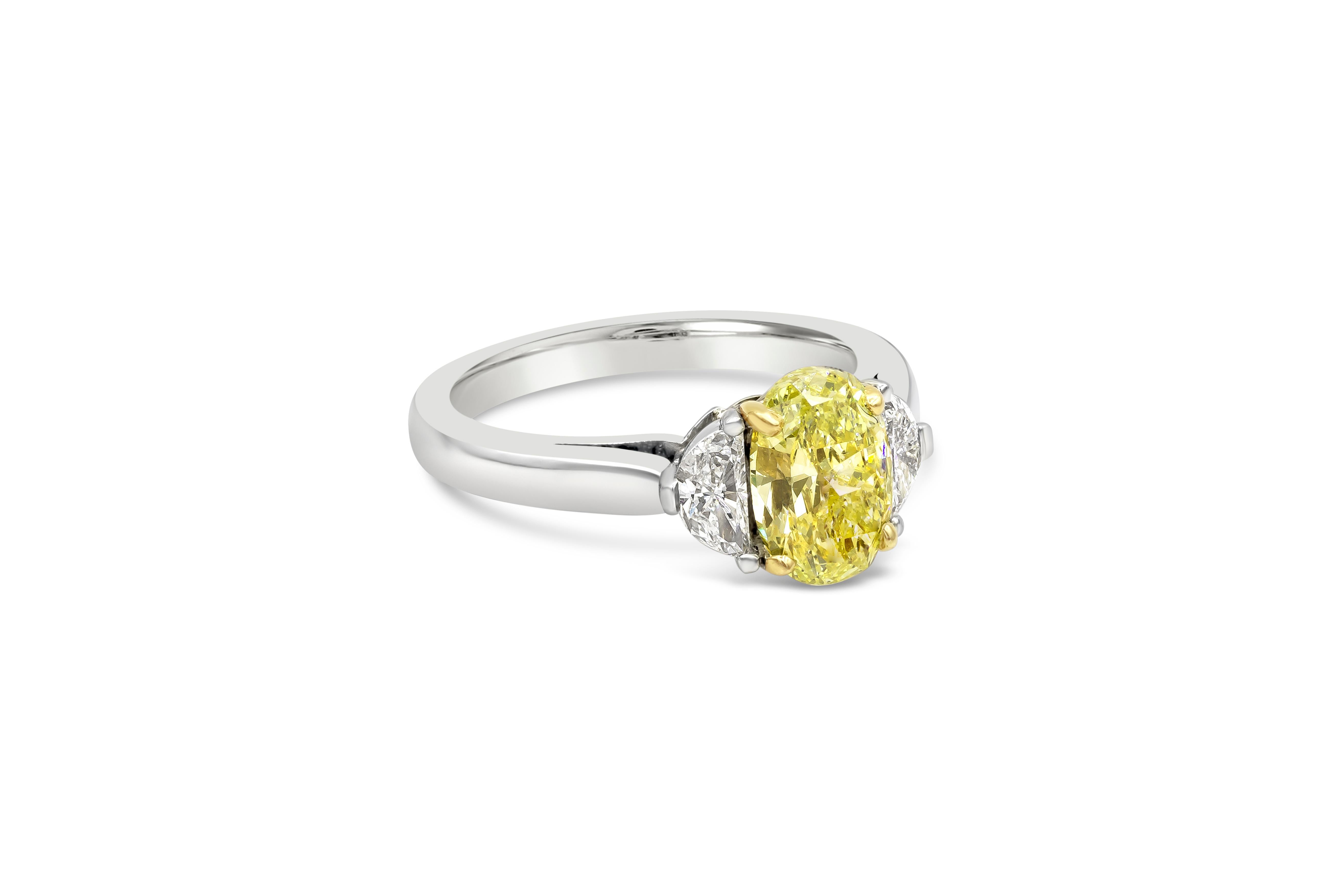 A classic three-stone engagement ring style showcasing a 1.50 carat color-rich oval diamond certified by GIA as fancy Intense Yellow color. Flanking the center are half moon diamonds on each side weighing 0.29 carats total. Set in a handcrafted