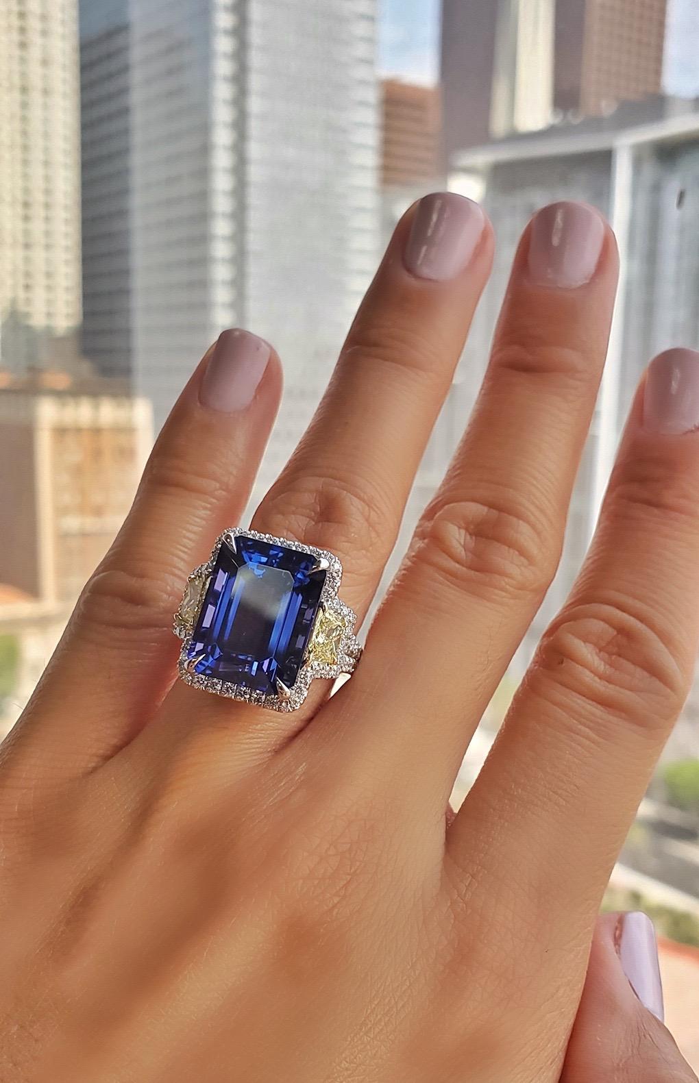 A Magnificent Modern Platinum Cocktail Ring set with a GIA Certified 13.82 Carat Natural Violet Tanzanite measuring 15.46x11.80x8.11mm. 

The trapezoid sidestones are GIA certified Fancy Yellow diamonds weighing 0.91 carats (0.45 & 0.46) and the