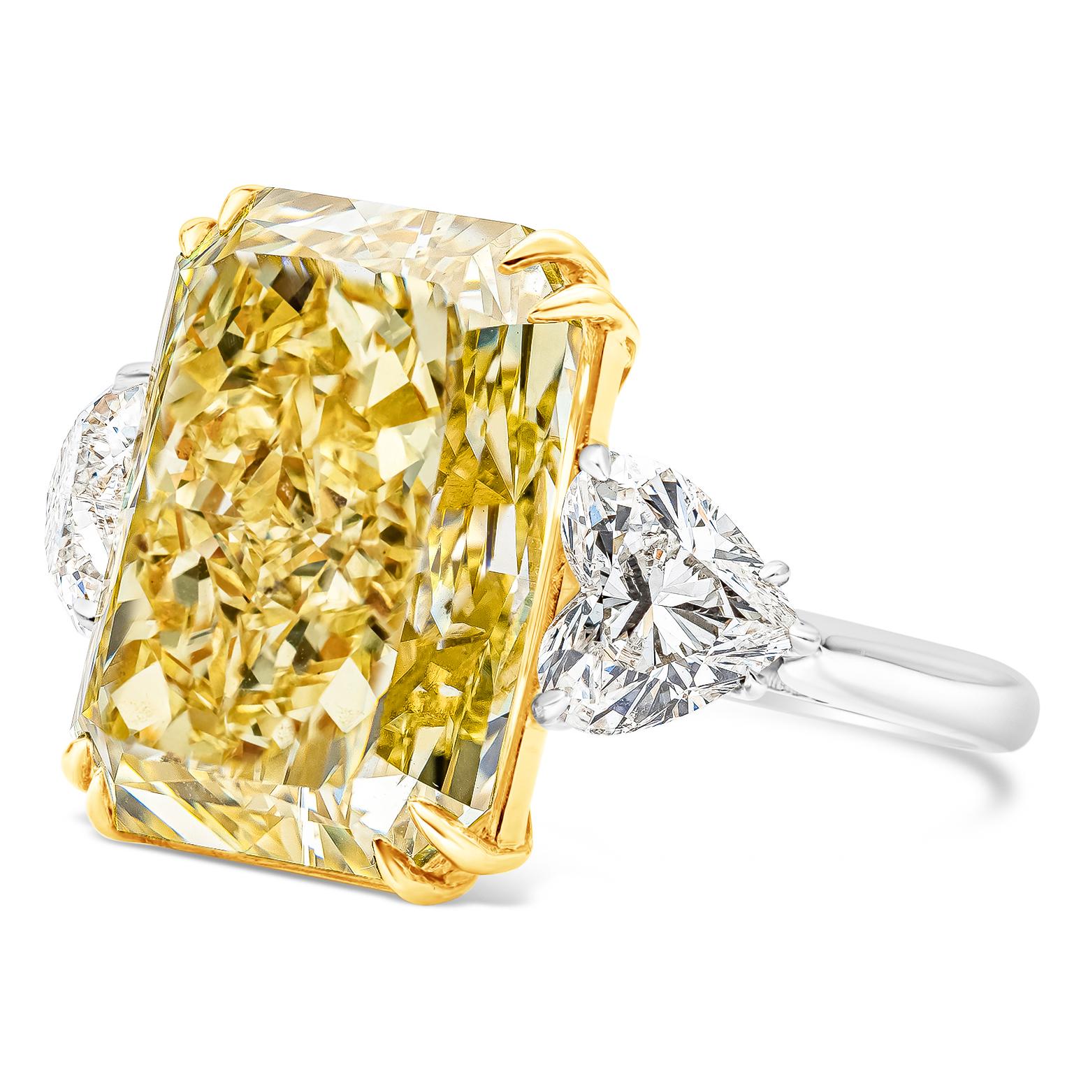 Rare and color rich three-stone engagement ring featuring a vibrant 17.25 carat elongated radiant cut diamond certified by GIA as fancy intense yellow, VS2 clarity, set in an eight prong 18K yellow gold basket. Flanking the center stone are