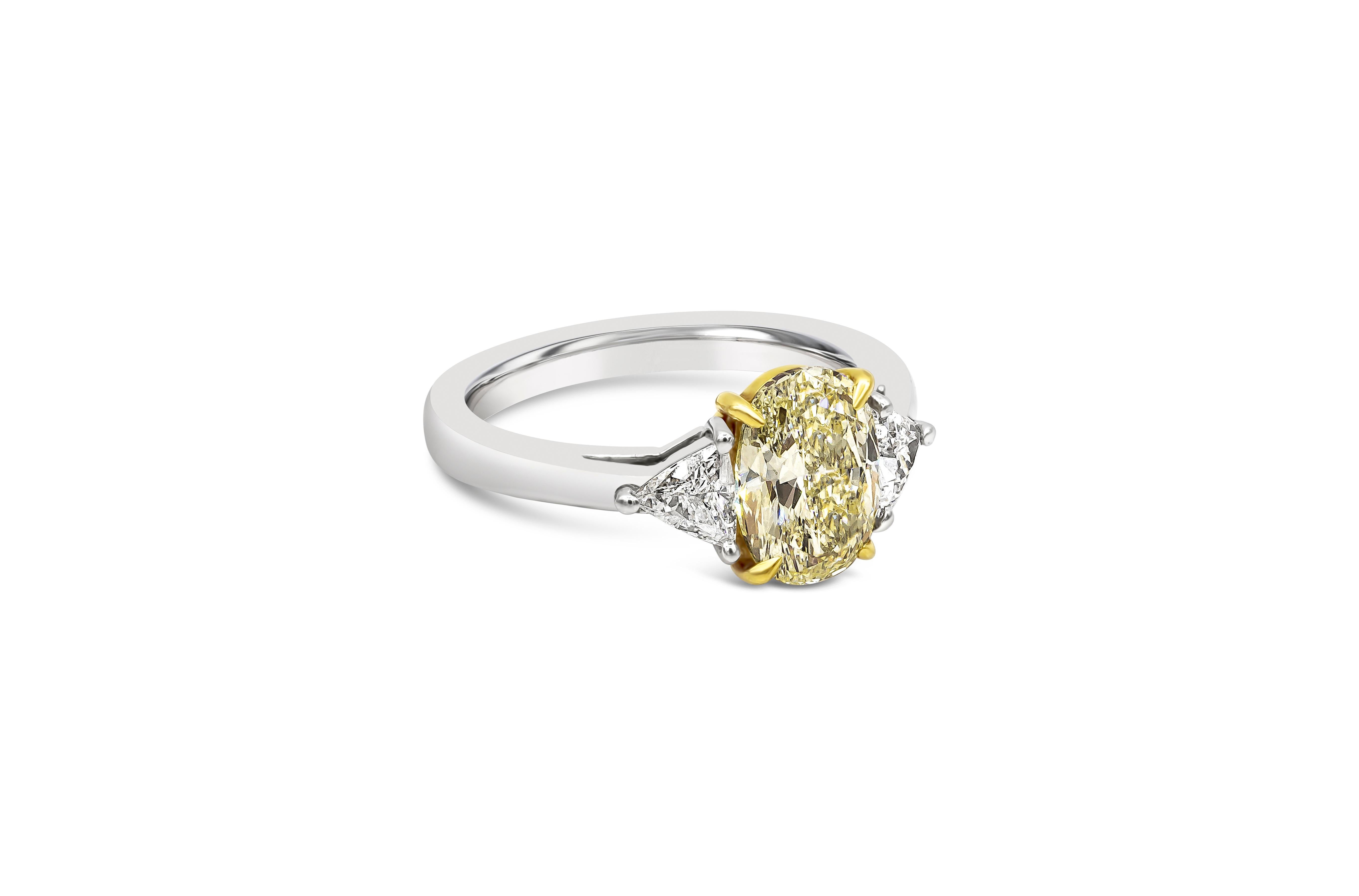 A contemporary three-stone engagement ring style, showcasing a 1.87 carat oval cut yellow diamond certified by GIA as Fancy Light Yellow color and SI1 clarity. Flanking the center diamond are two brilliant cut trillion diamonds weighing 0.47 carats