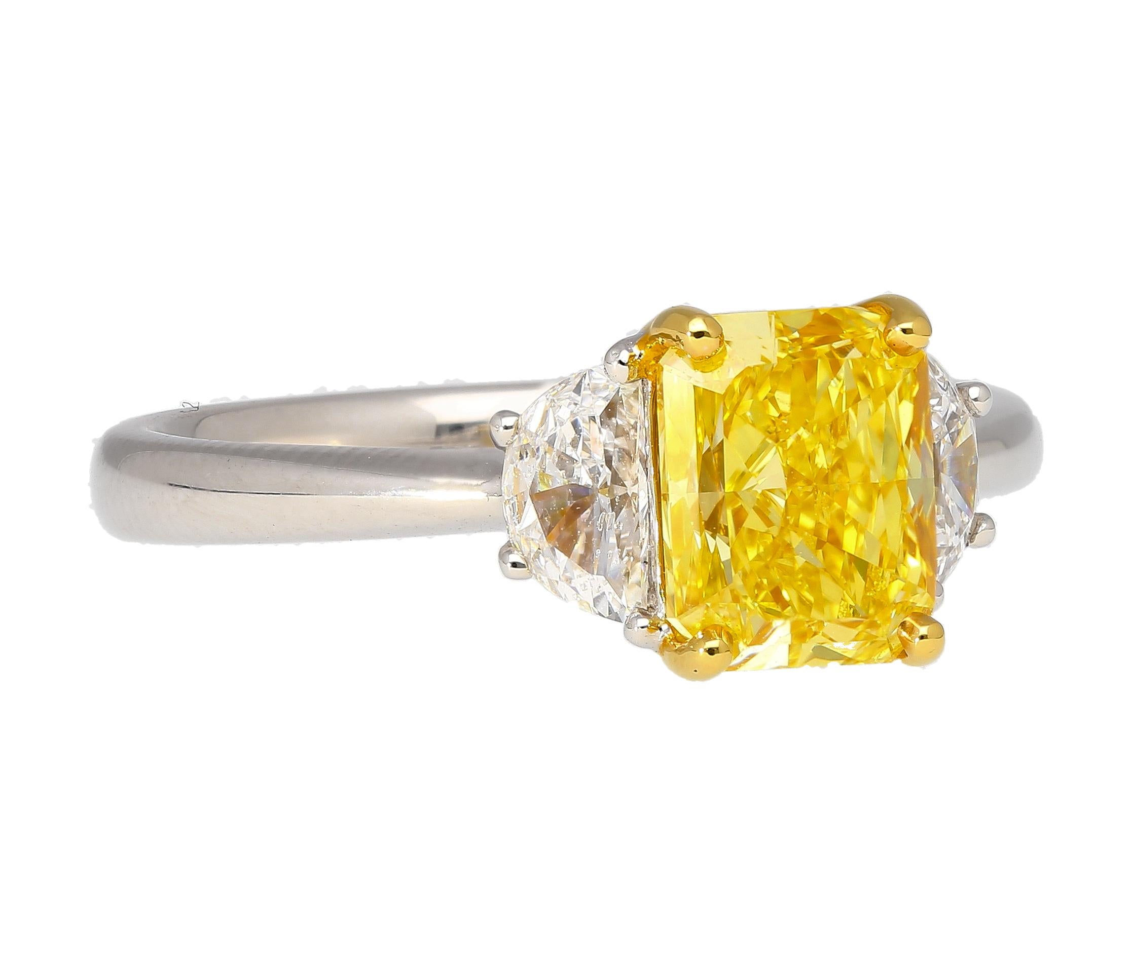 Prepare to be mesmerized by the extraordinary beauty of this three stone engagement ring, featuring a GIA certified 2.01 carat fancy vivid yellow radiant cut diamond center stone. Flanked by two half-moon cut F color diamond side stones. Set in 18K
