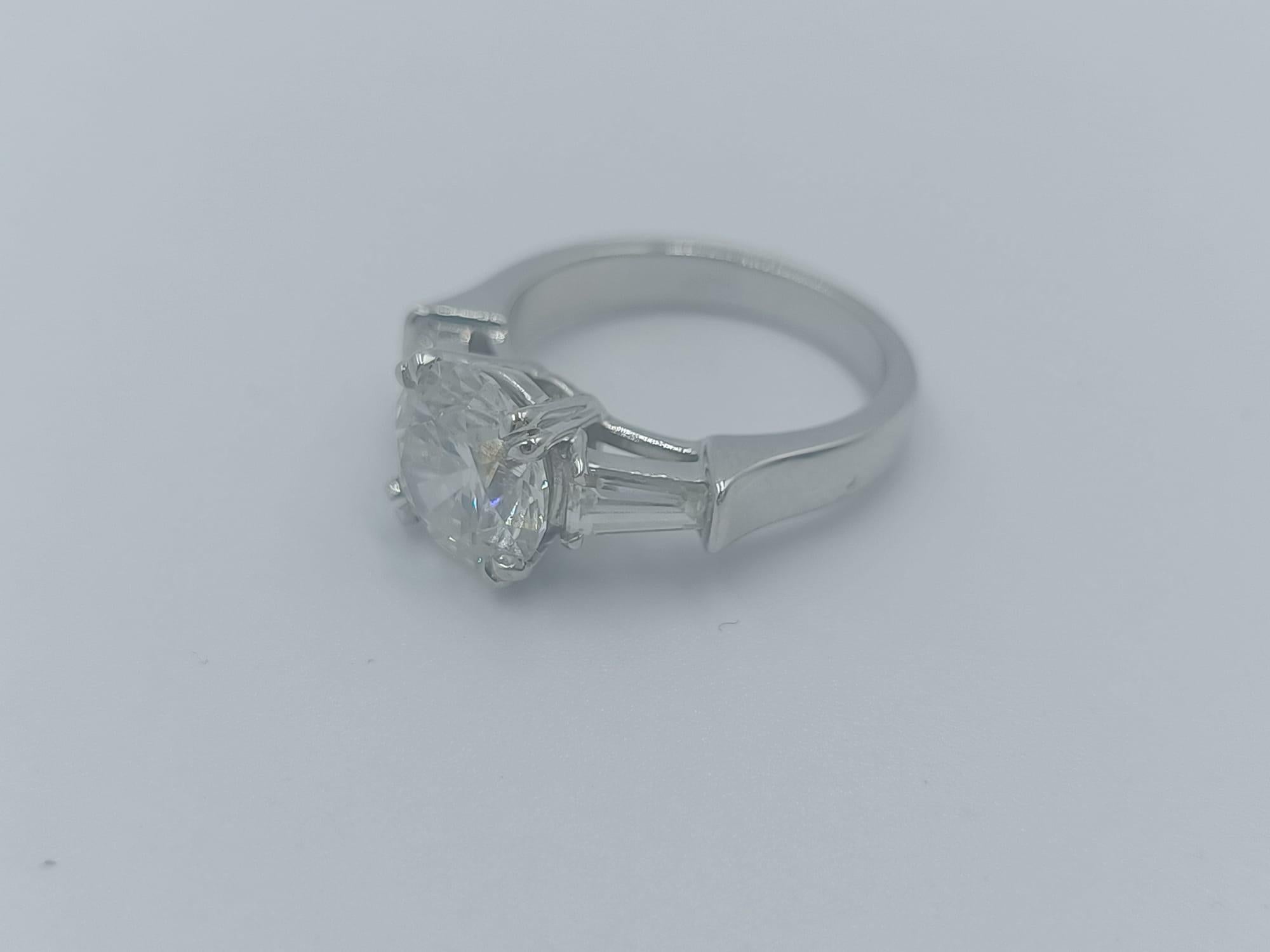 Cette bague exquise met en valeur un diamant rond de 2.11 carats taillé en brillant comme pièce maîtresse, rayonnant d'une élégance intemporelle et d'une brillance inégalée. 

Certifié par le GIA, le diamant est de couleur E, ce qui lui confère un