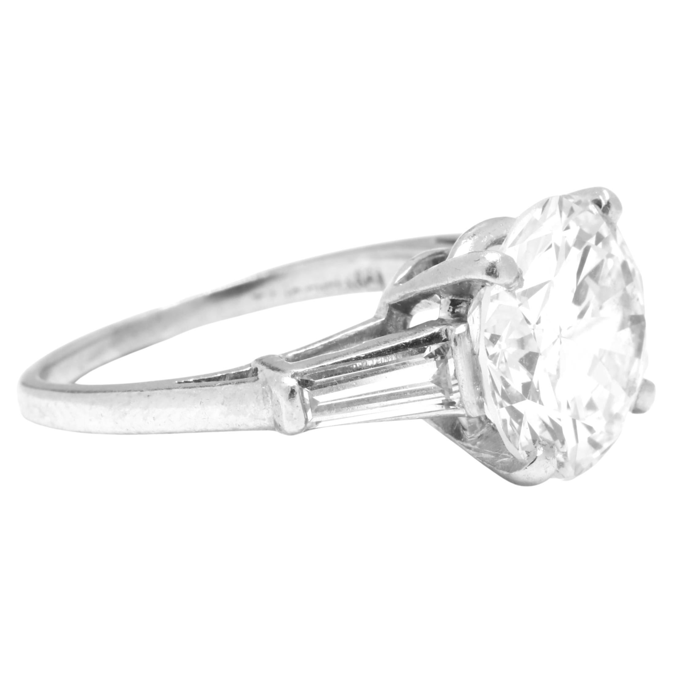 This exquisite ring features a dazzling 2.28 carat round cut diamond, accented by two elegant tapered baguette diamonds, all set in luxurious 18K White Gold. 

E level color quality ensures this diamond radiates elegance with a nearly flawless icy