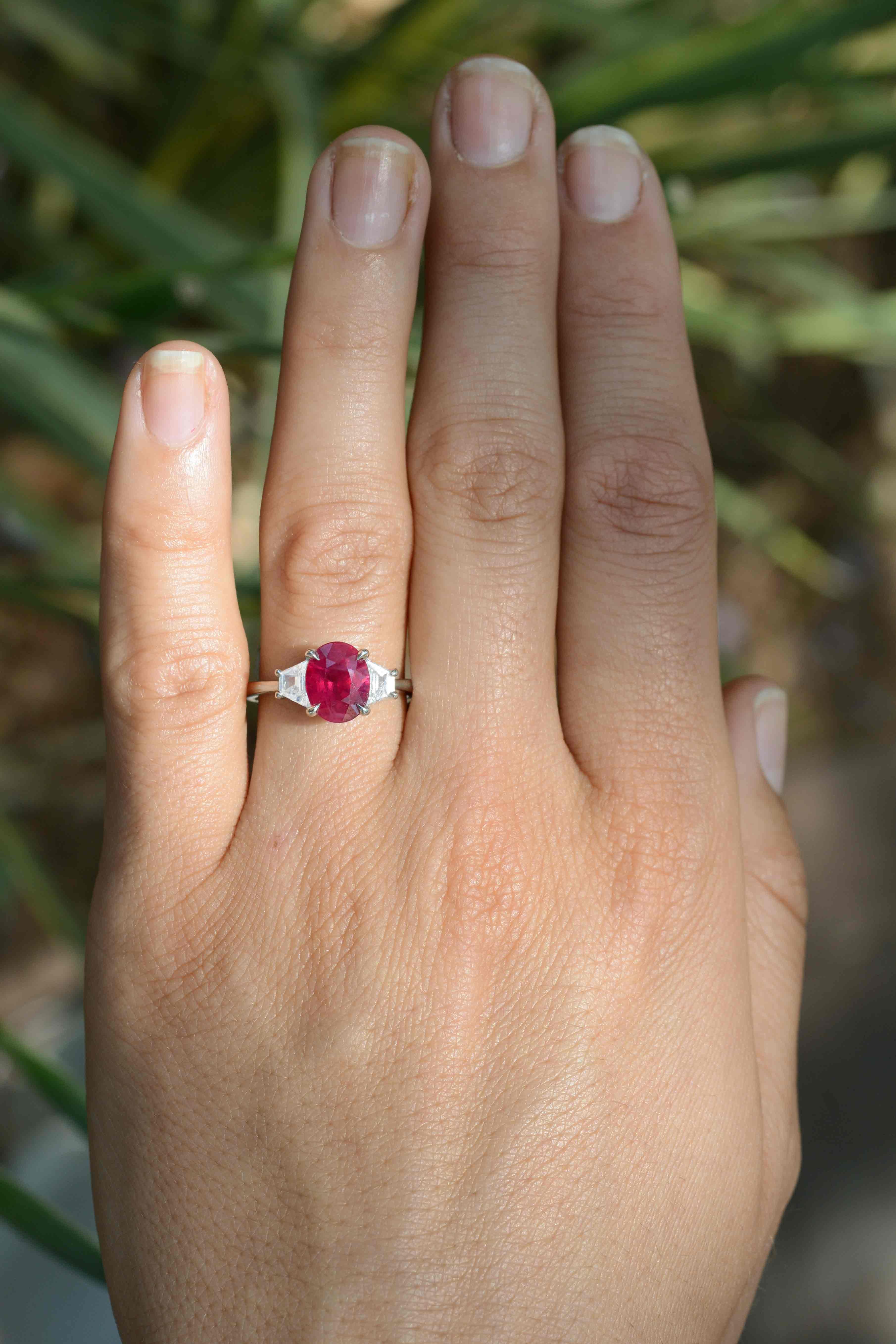 The Beaumont natural ruby engagement ring is centered by a vivid, pigeon blood red oval ruby certified by the Gemological Institute of America. A classic, 3 stone platinum mount featuring elegant claw prongs is accented by a pair of dazzling
