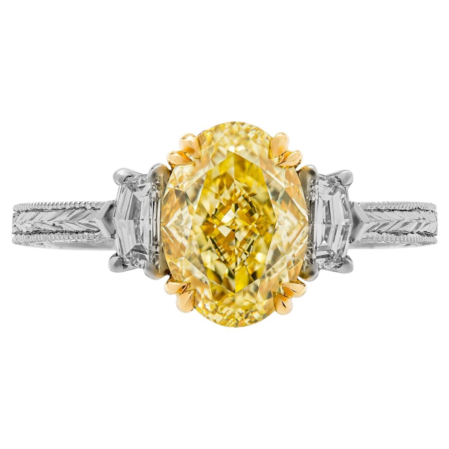 Fancy 3 stone ring in 18K & Pt950;
 Filigree shank; diamond basket under center stone;  
TCW of melee: 0.15ct 
Side stones: 0.44ct (total)  Cadillac shape diamonds; 
Center Stone: Oval 2.40ct Natural Fancy Yellow, VVS1, GIA#6302448878

Comes with