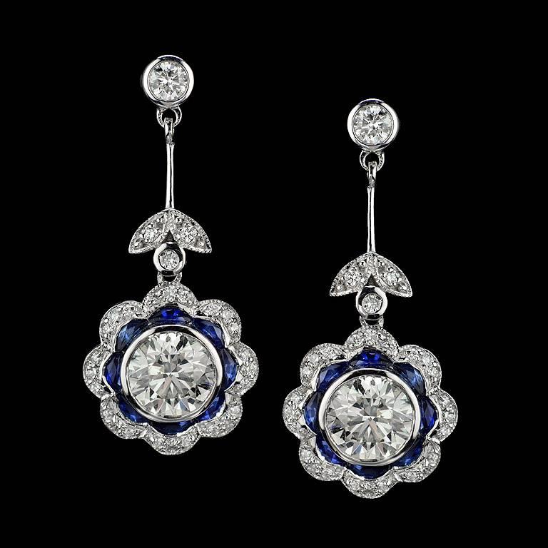 A perfect pair of round brilliant-cut Diamonds Dangles earrings setting with...
1. GIA Certified 1.23 Carat Weight Diamond L Color VS2 Clarity
2.GIA Certified 1.21 Carat Weight Diamond L Color VS1 Clarity
Both are surrounded by French Cut Thai Blue