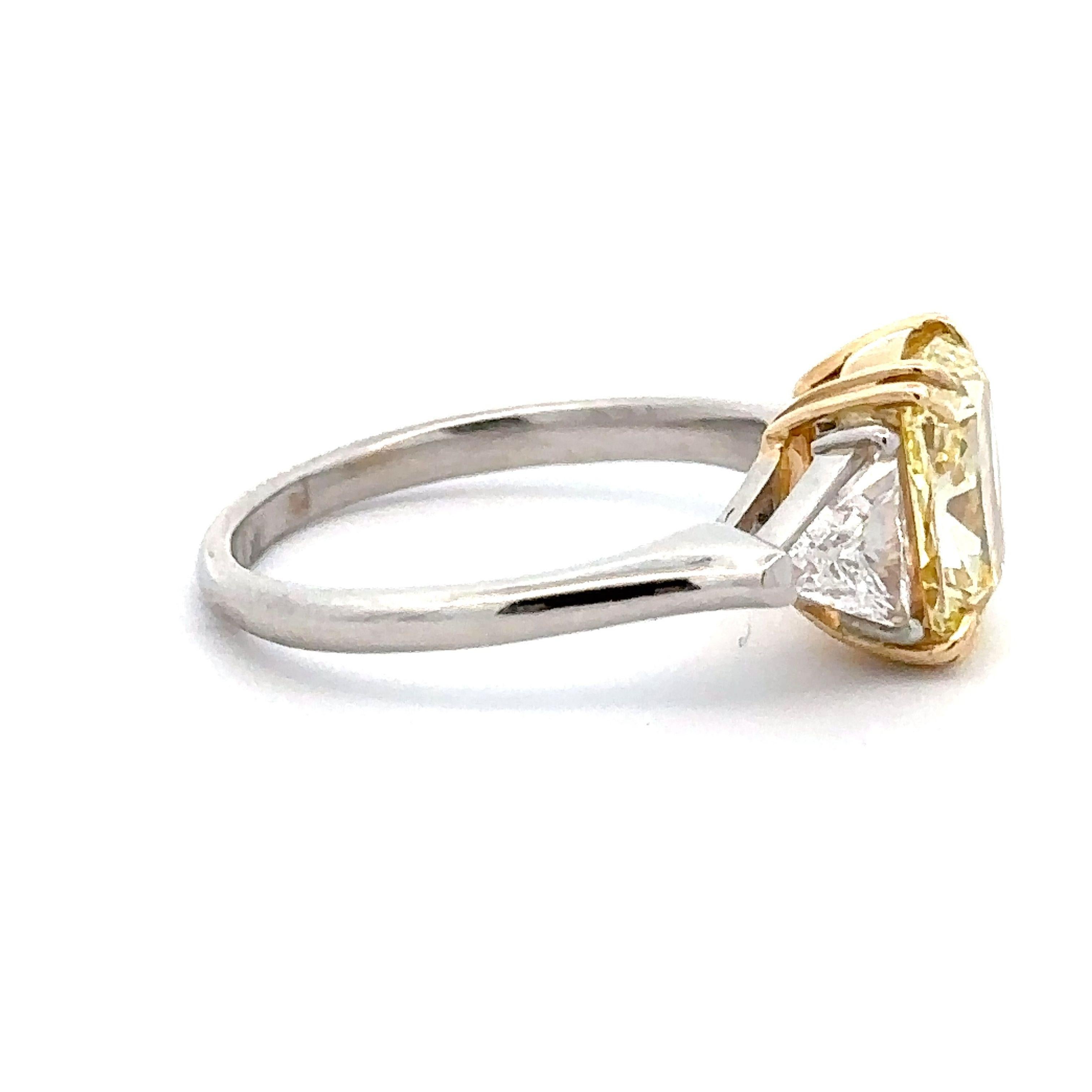 Introducing a 2.58 carat Fancy Yellow VVS2 G.I.A certified  Cushion Cut center diamond flanked by Trillion Cut diamond weighing 0.40 carat, This 3 stone ring is a captivating masterpiece that transcends the boundaries of elegance and sophistication.
