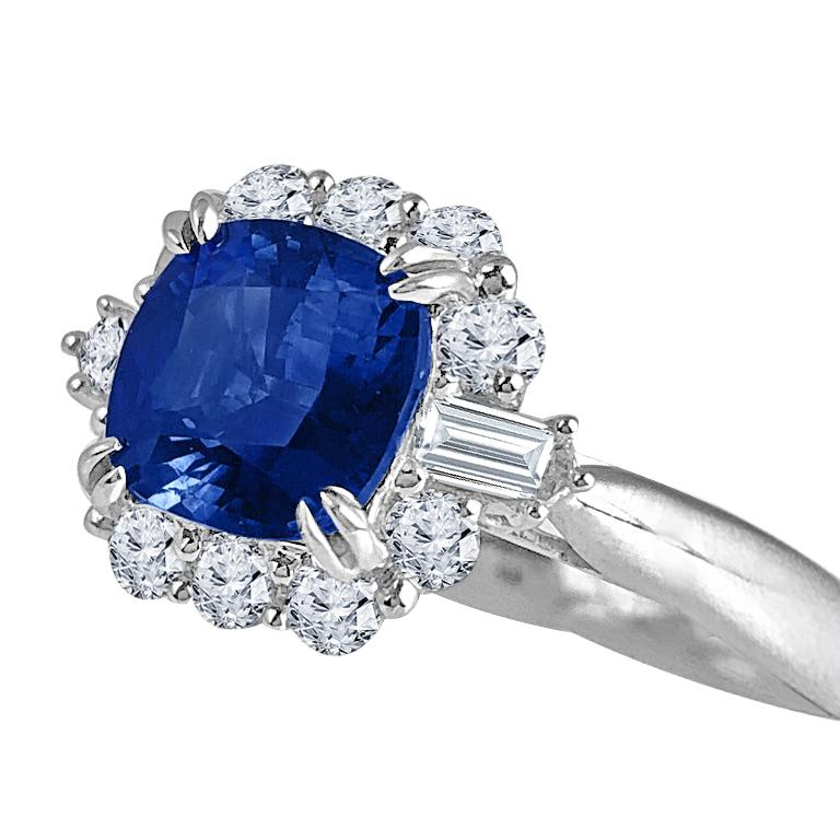 Dieser faszinierende Ring zeigt einen atemberaubenden GIA-zertifizierten blauen Saphir von 2,60 Karat im Kissenschliff, der von einem brillanten Halo aus runden natürlichen Diamanten umgeben ist. Zwei Baguettes aus natürlichen Diamanten, die sich