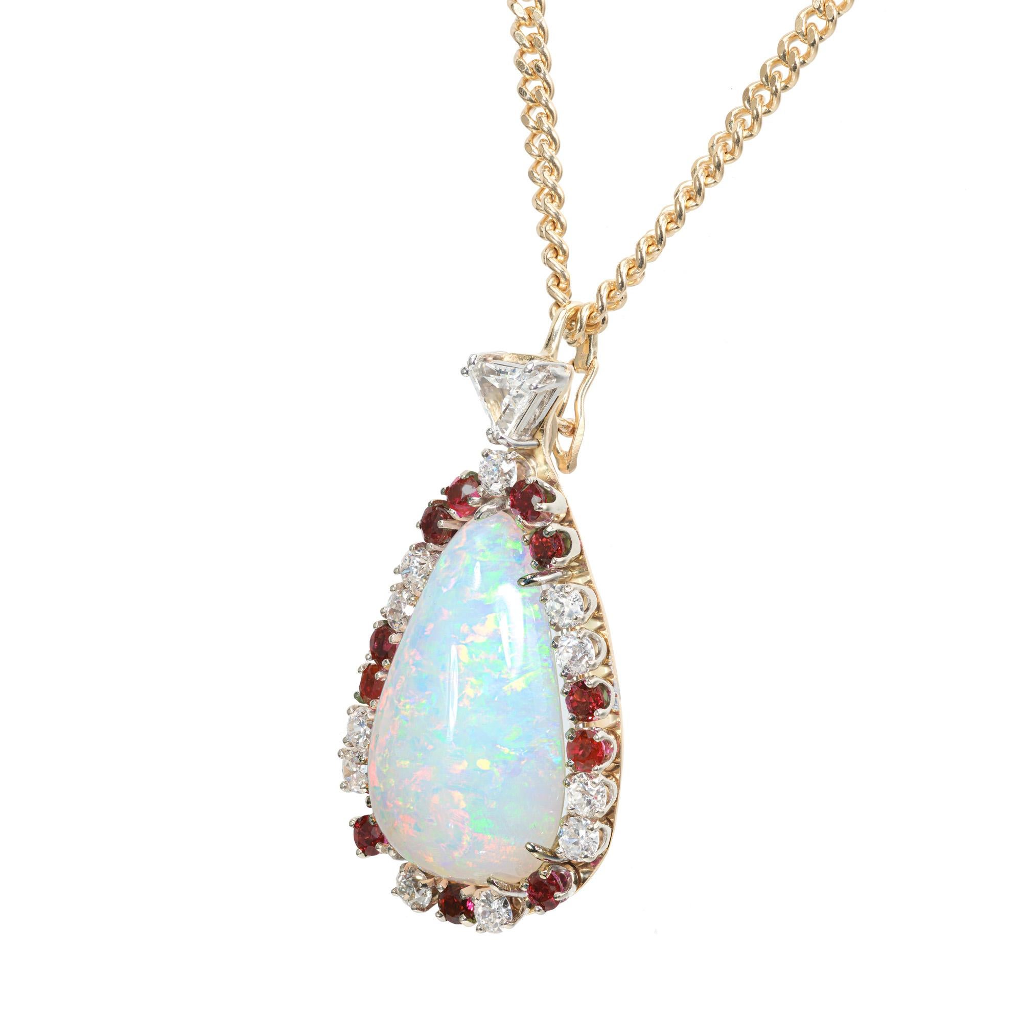 1960's Opal, ruby and diamond pendant necklace. GIA certified 27.03 carat pear shape opal with a halo of 11 round diamonds and 11 round rubies. Accented with 1 trilliant cut diamond in a 14k yellow and white gold setting with a 22 inch yellow gold