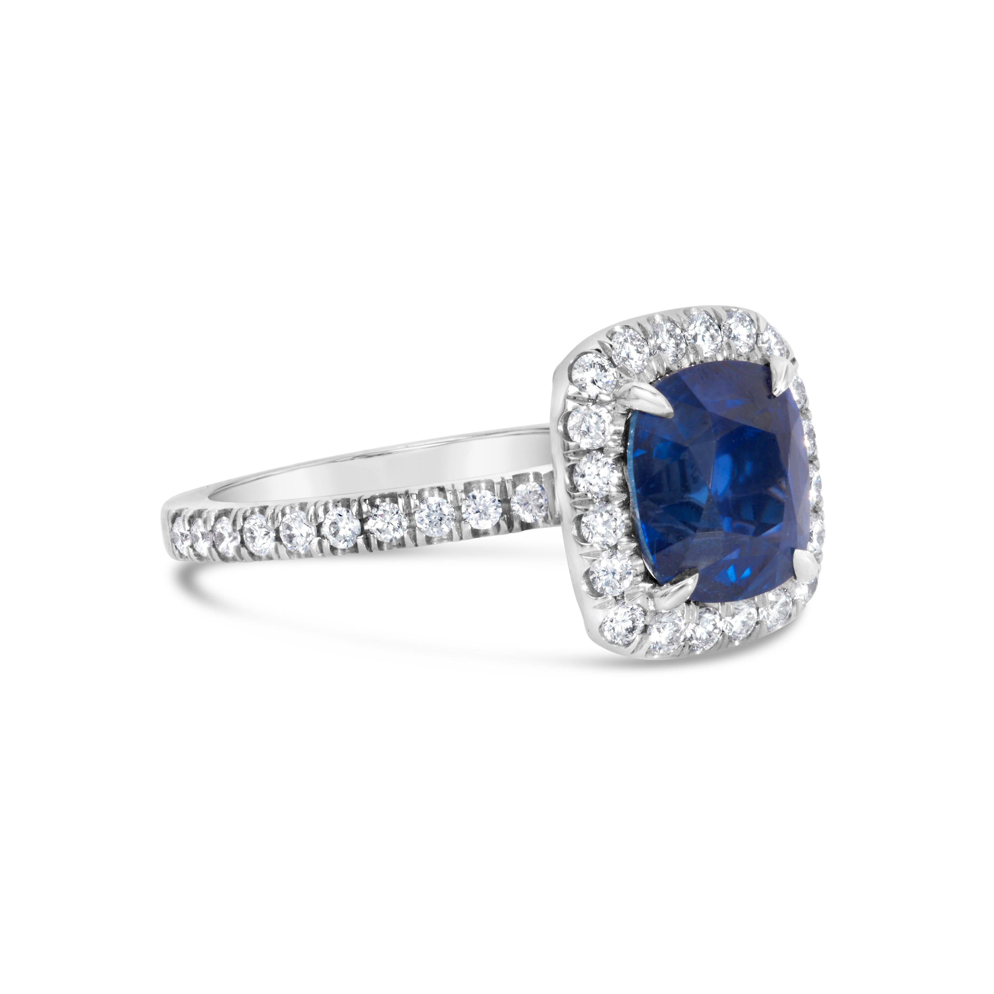 A gorgeous engagement ring, showcasing a 2.75 carats cushion cut sapphire certified by GIA as Blue color with no indications of heat treatment, set on a four prong setting. Surrounded by a halo of sparkling round brilliant cut diamonds and accented