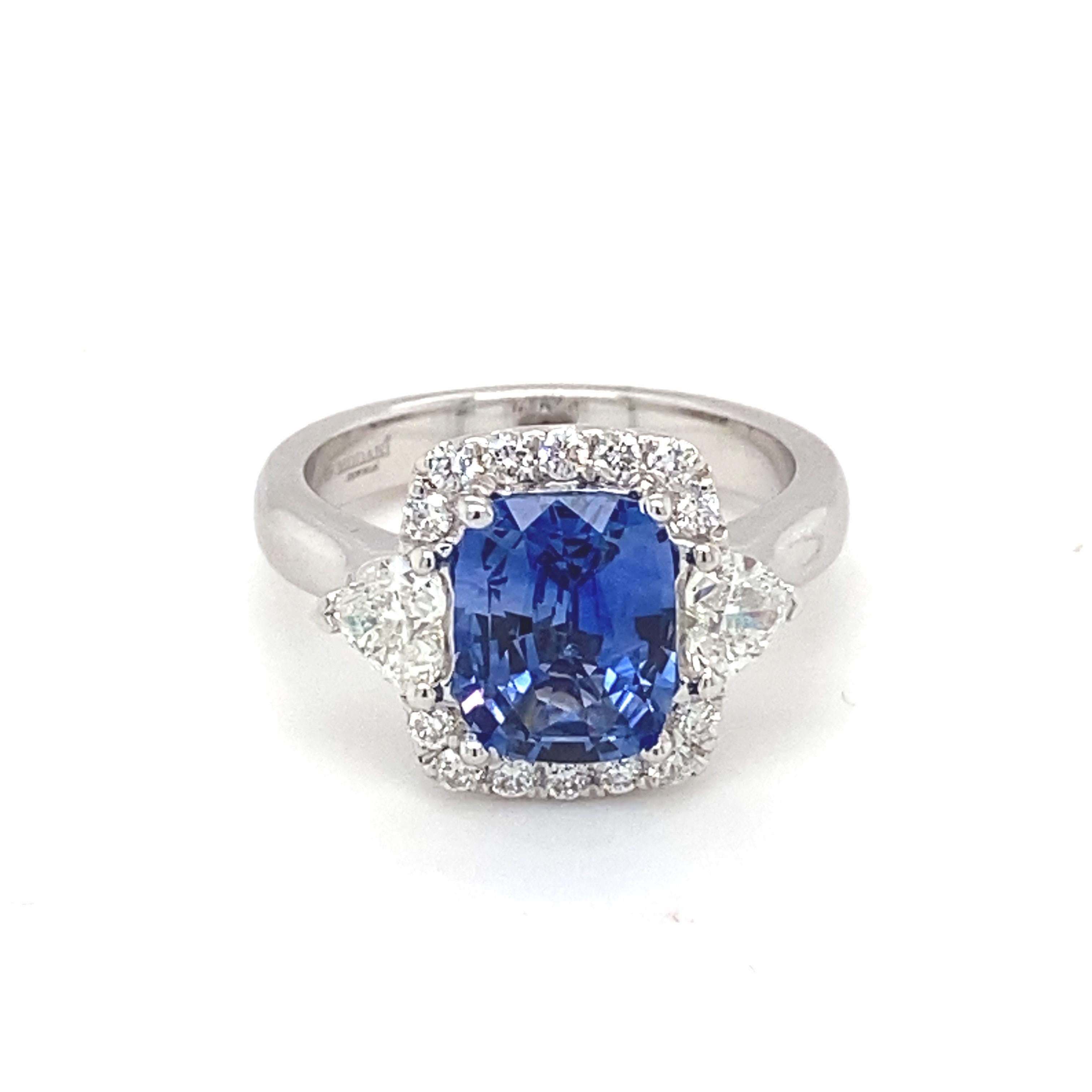 This GIA Certified 2.76 carat blue sapphire cushion shape center stone is surrounded by a glittery halo of white diamond. It also has two trillion shape white diamond as side stone. This exceedingly elegant ring mounted in white gold dazzles with