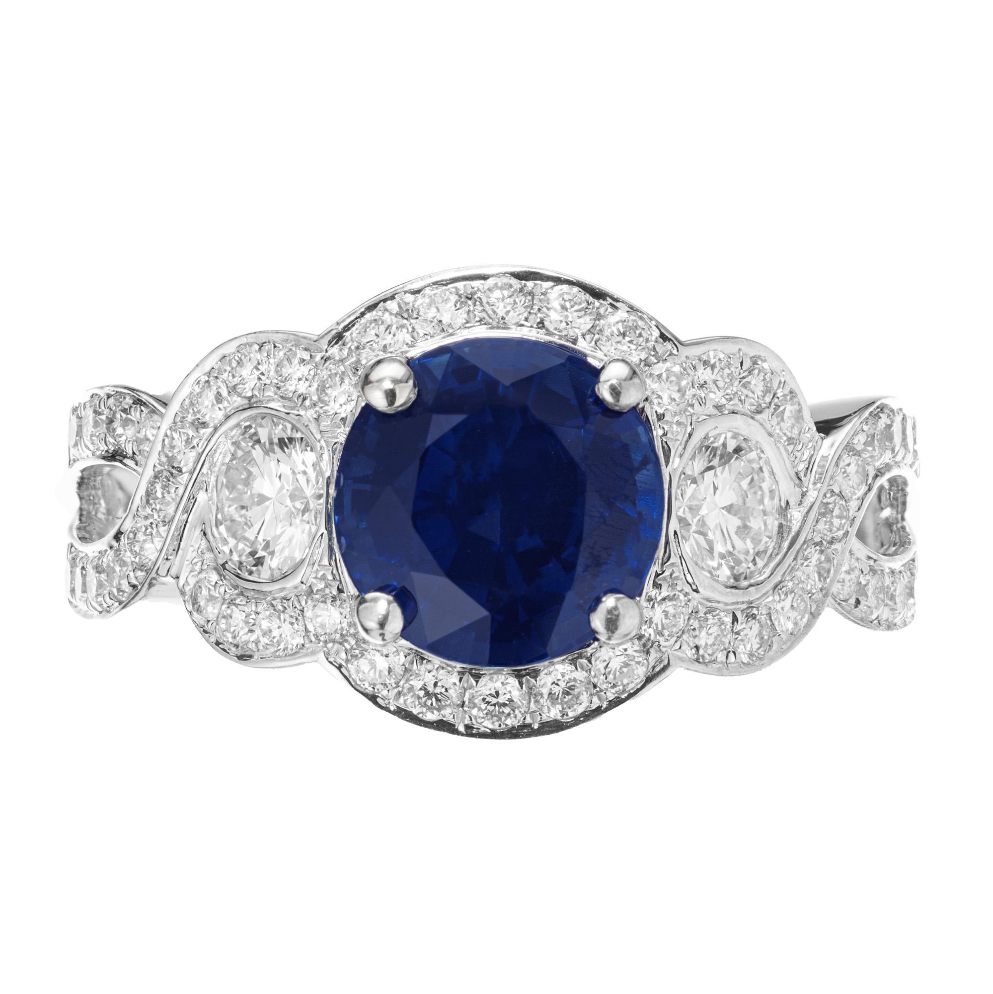 Royal Blue Round Sapphire Diamond Swirl engagement ring. This rich blue GIA certified sapphire is set in a swirl design 18k white gold setting. The center sapphire is accented with two round cut diamonds and surrounded by a halo of round diamonds