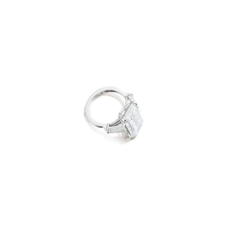 This exquisite engagement ring showcases a 3.01 carat emerald cut diamond as its centerpiece, set in elegant 18K white gold. The three stone setting symbolizes past, present, and future, making it a meaningful choice. It's sleek and refined design