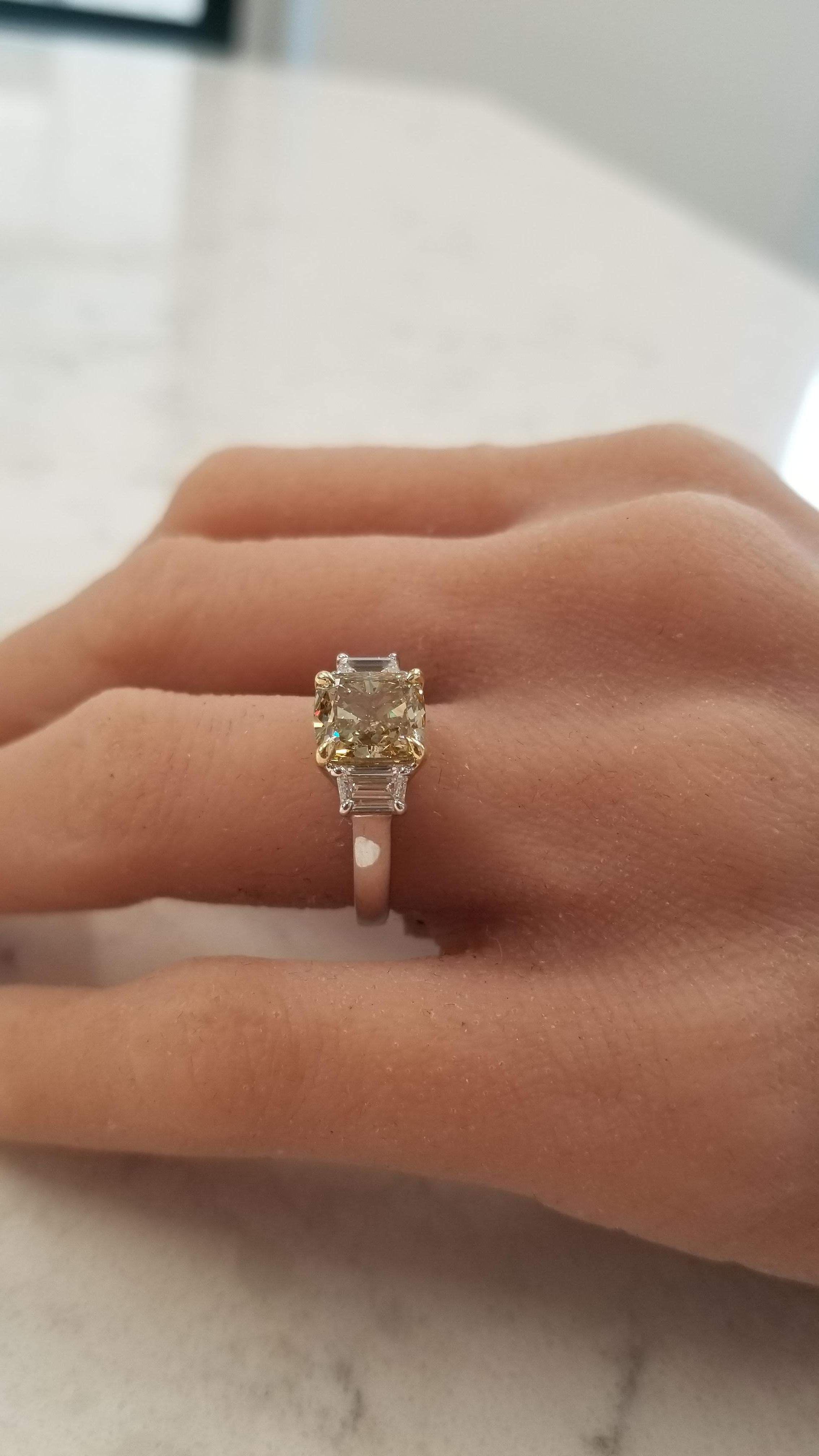 This special three stone ring features a 3.00 carat cushion cut fancy brownish yellow diamond in a rich yellow gold prong setting in the center. The color resembles a mix of golden honey and cinnamon. This gorgeous center stone is flanked by two
