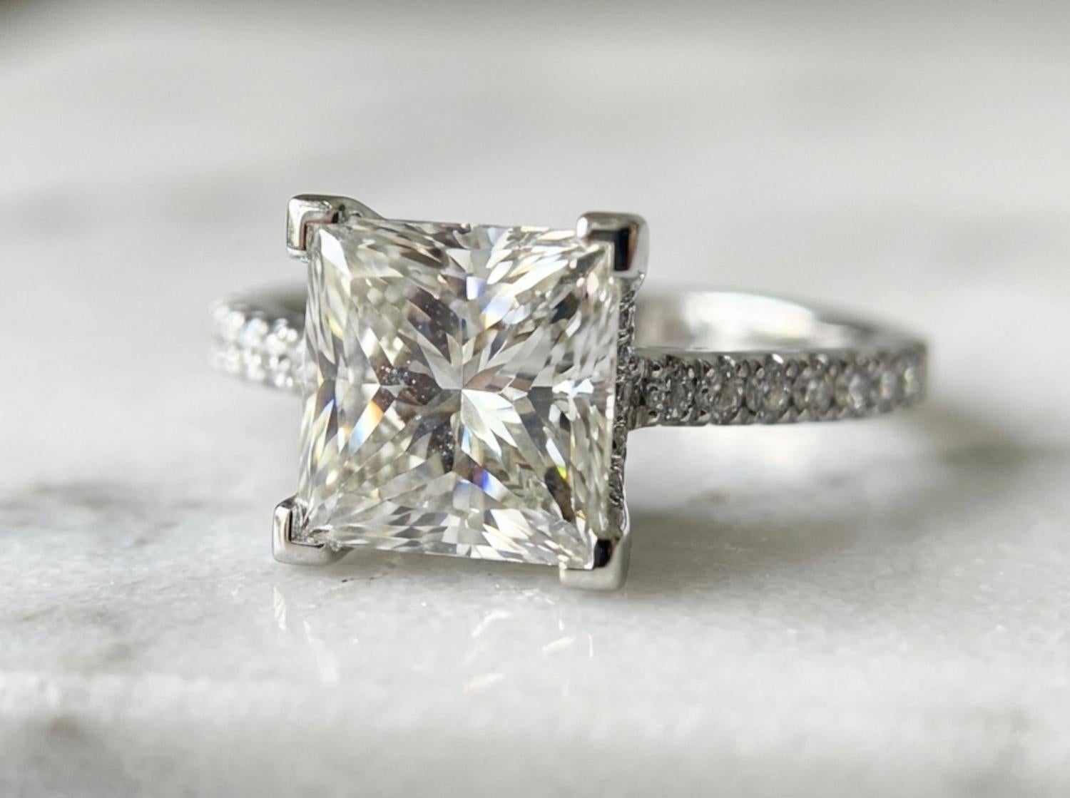 Cette exquise bague de fiançailles en platine met en valeur un superbe diamant de 3,00 carats de taille Princesse (Rectangular Modified Brilliant), certifié par le GIA de couleur E et de pureté VS1.
La pierre présente une luminosité exceptionnelle,