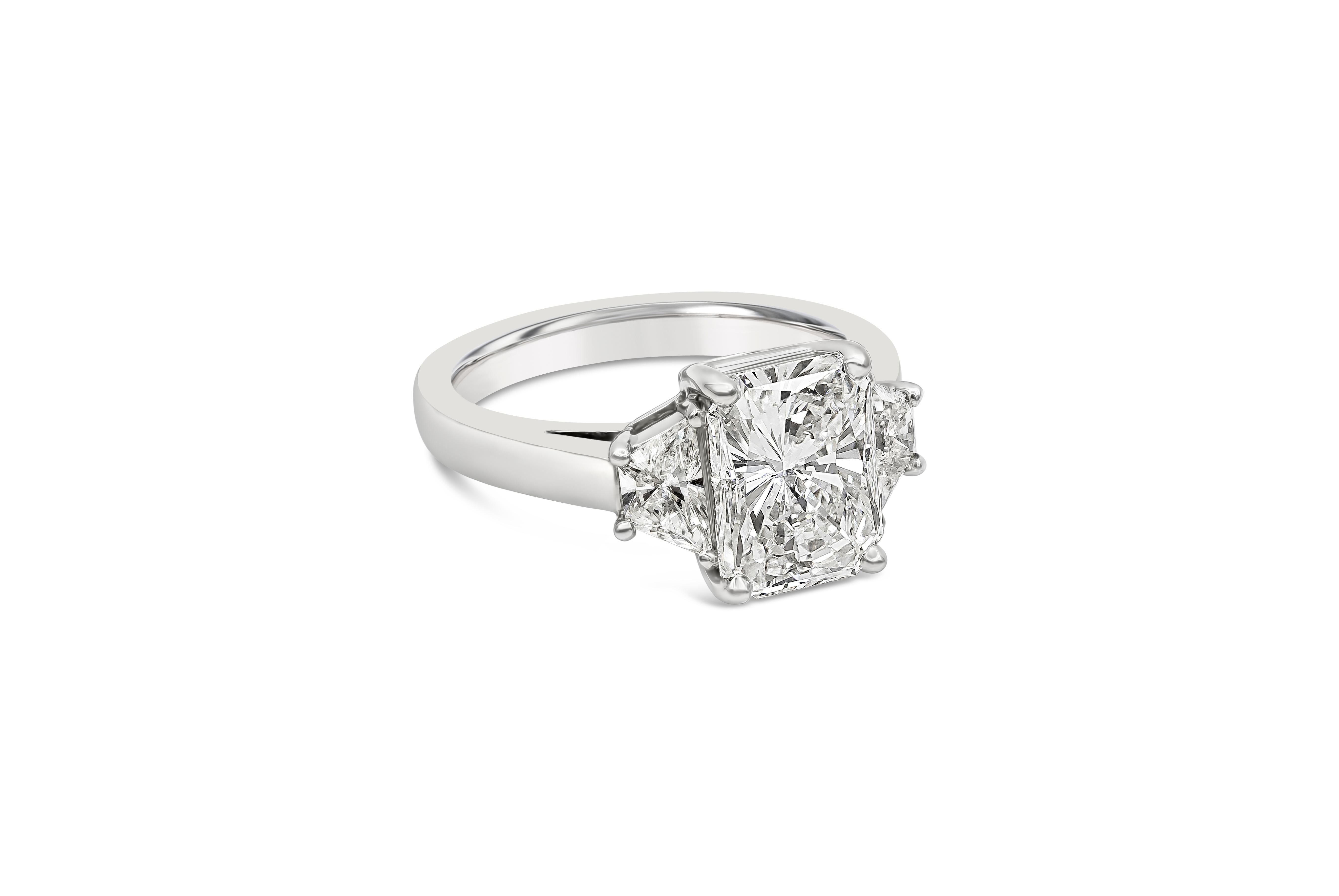 An elegant three-stone engagement ring, showcasing a 3.00 carats radiant cut diamond certified by GIA as H color and VS1 clarity, set on four rounded prongs. Flanked by brilliant trapezoid cut diamonds weighing 0.66 carat total. Finely made with a
