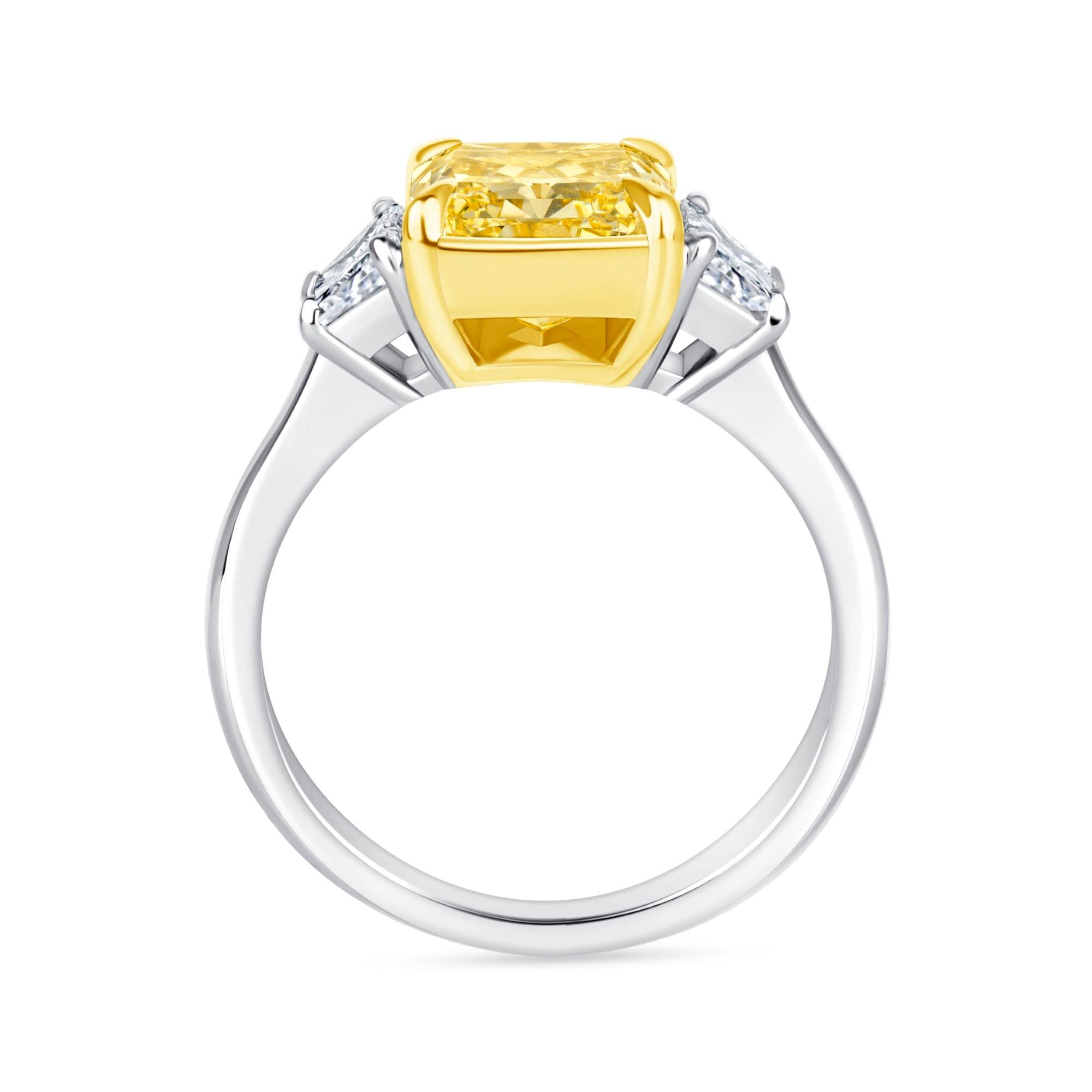 This three stone ring has a 3.00 carat Fancy Intense Yellow Radiant cut diamond in GIA certified in VS1 clarity and two Brilliant Trapezoid shape diamonds, E -F in color, VS1 in clarity set in 18K Yellow Gold and Platinum.  It has an approximately