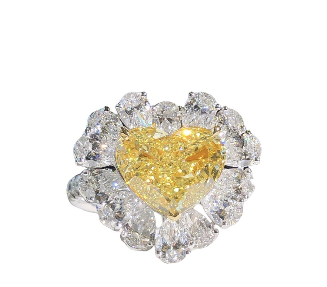 Entdecken Sie diesen eleganten und majestätischen Cocktailring mit einem 3,02 Karat GIA-zertifizierten Diamanten im Fancy Yellow Heart-Schliff, der von farblosen Diamanten im Birnenschliff akzentuiert wird. Dieser Ring im romantischen Stil ist der