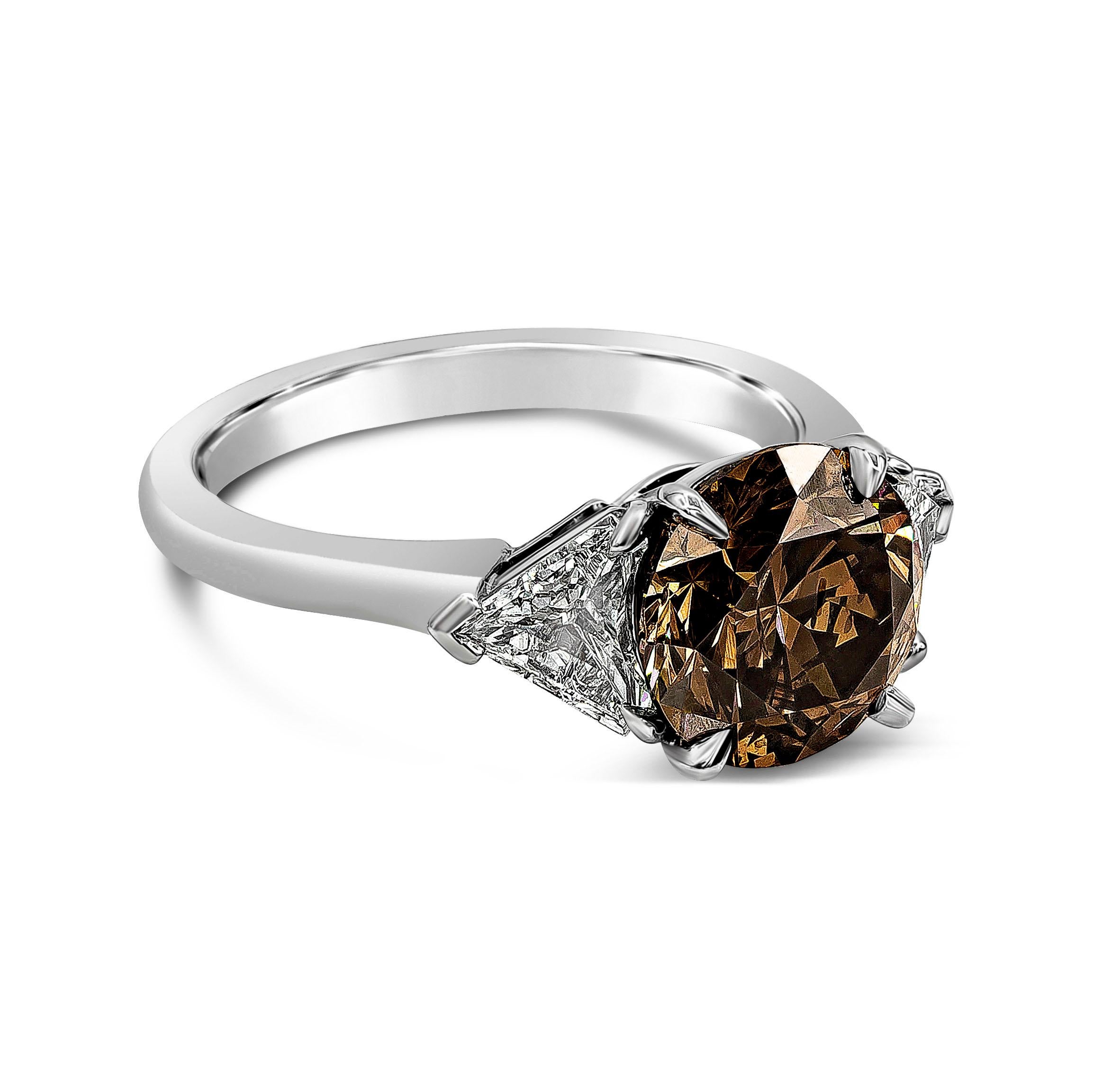 A unique diamond stone engagement ring, showcasing a 3.04 carats round brilliant cut diamond certified by GIA as Fancy Dark Orangey Brown color and SI2 clarity, set on a four claw prong basket. Flanked by two gorgeous trillion cut diamonds weighing