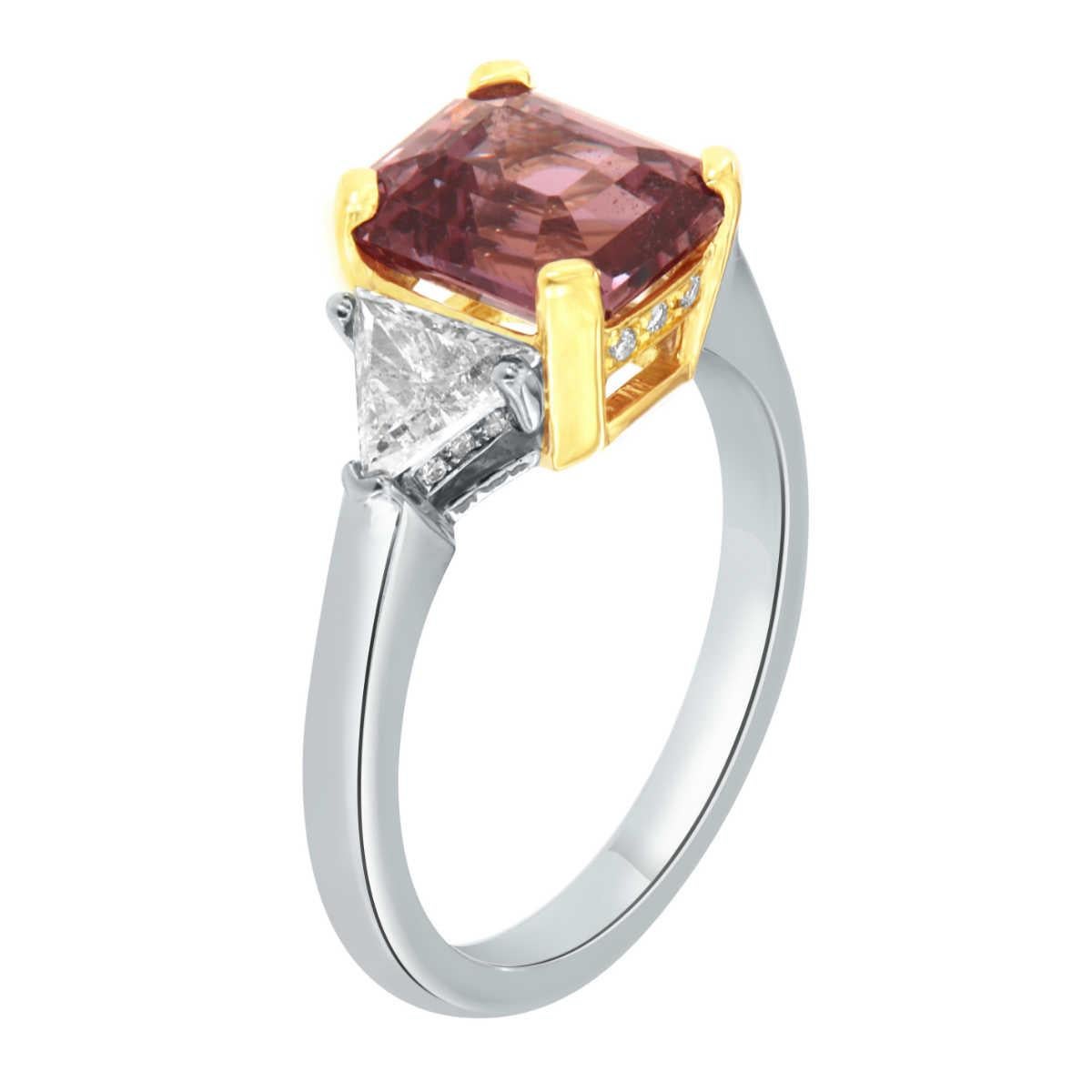 This magnificent three-stones 18k & 14K Two-Tone gold ring features three gems. The center is a 3.21-carat Emerald cut Natural Purplish- Pink Natural sapphire flanked by two Trillion cut diamonds in a total weight of 0.50 carat. A hidden row of