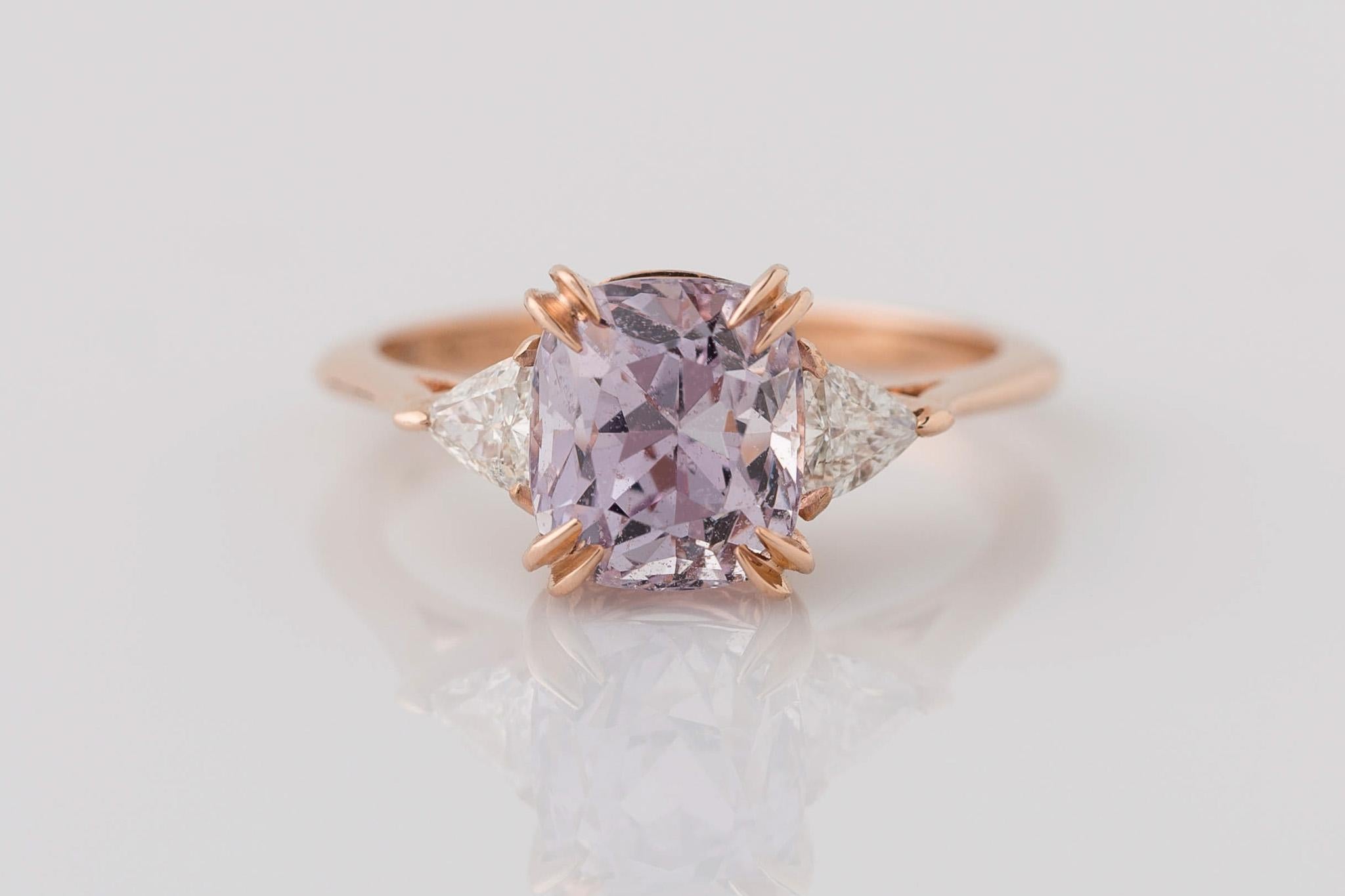 Indulge in elegance with our 14K Rose Gold GIA Certified 3-Stone Cushion Cut Pink Sapphire Ring. The centerpiece, a GIA certified 3.28 Ct. unheated sapphire, boasts a captivating light lilac purple hue with transparent clarity. Accompanying the