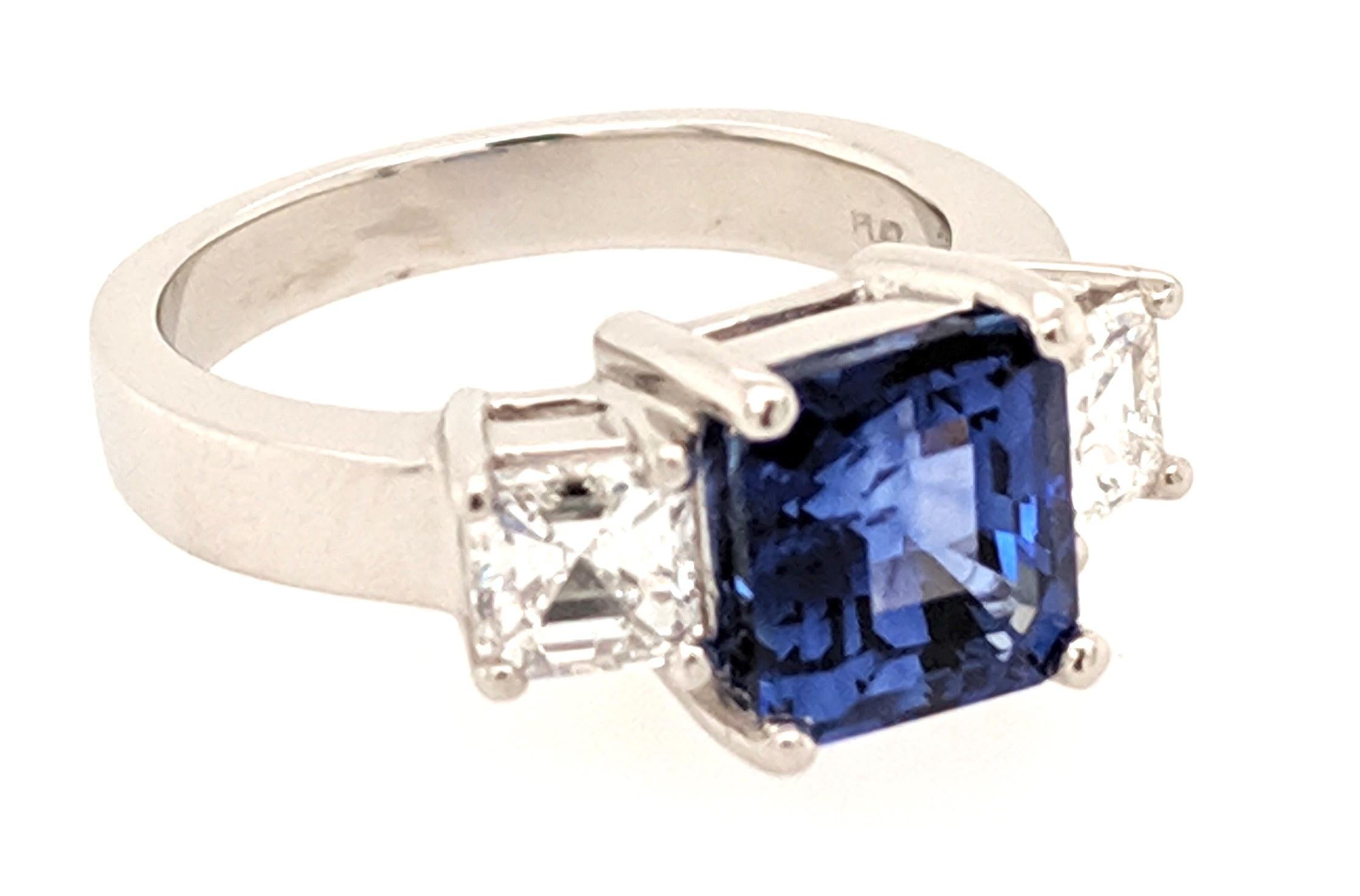 A 3 Stone Sapphire and Diamond Ring crafted in Platinum and Featuring (1) Asscher cut royal blue Sapphire from Madagascar weighing 3.31ct flanked by (2) Asscher cut diamonds weighing 1.01cttw with a color of F/G and a clarity of VS1. The ring is a