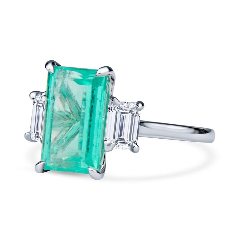 This phenomenal cocktail ring features a 3.32 carat GIA certified octagonal step cut Colombian emerald accented by 0.74 carat total weight in emerald cut natural diamonds on each side. It is set in 18 karat white gold. It is a size 6 but can be