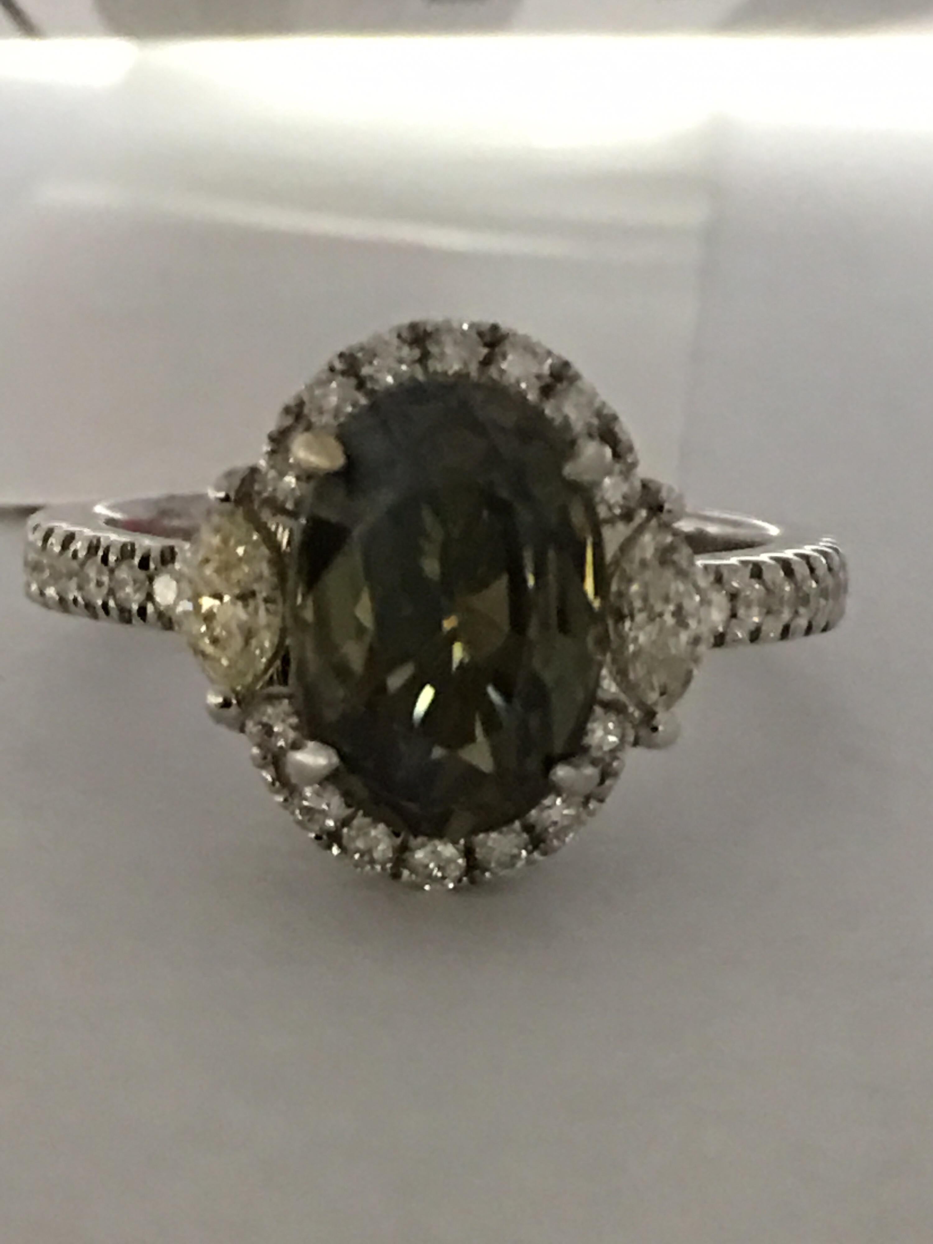 Natural GIA Certified 3.35 Carat Alexandrite which color changes from yellowish to greenish-brownish is natural stone set in 18 Karat white gold. Total weight 0.57 Carat Diamond around Alexandrite enhance the beauty of the ring.Size of the ring is 7