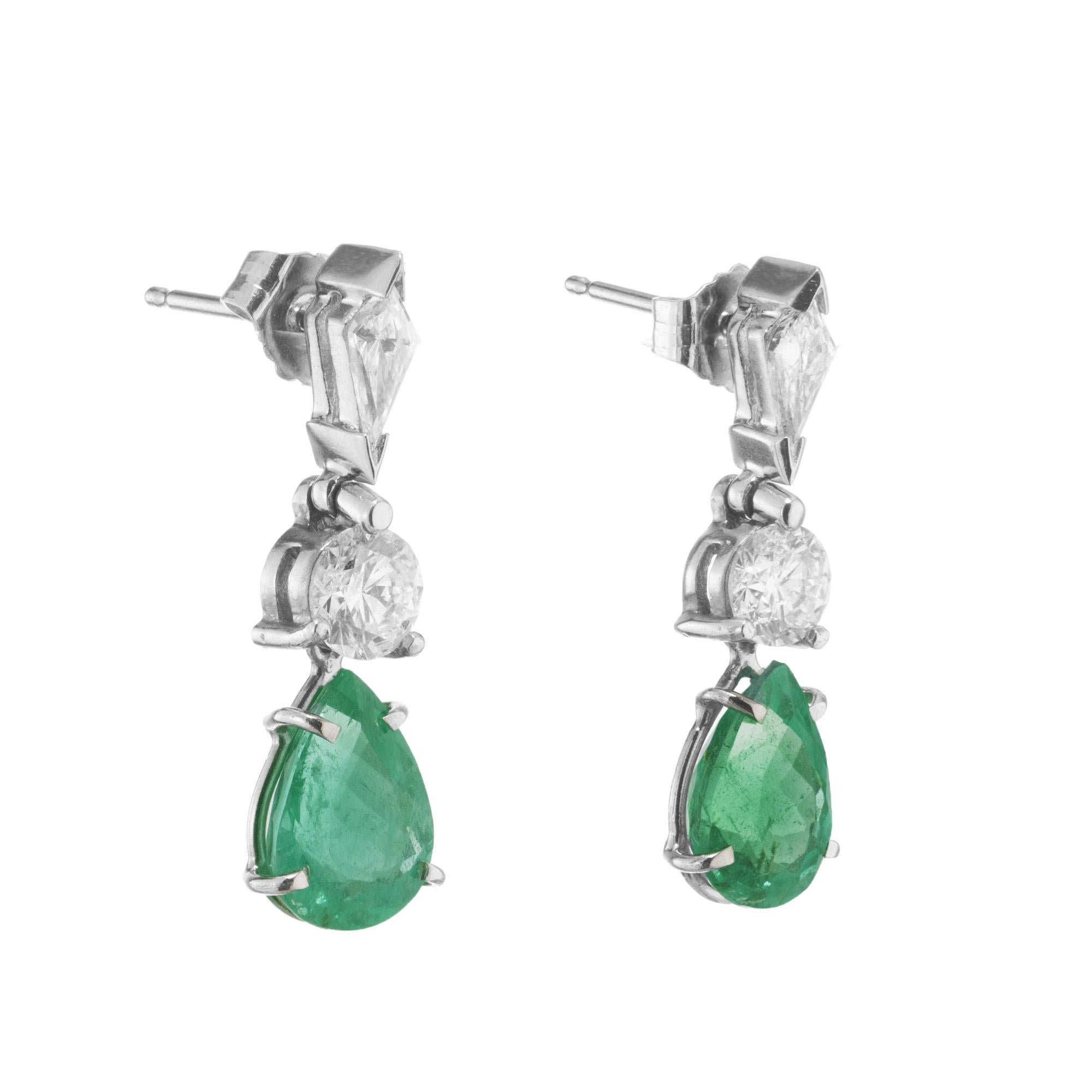 Emerald and Diamond Platinum dangle earrings. These earrings begin with two kite shaped diamonds followed by two round cut diamonds mounted in platinum upper dangles. The lower dangles are set with pear shaped emeralds, one with a carat weight of