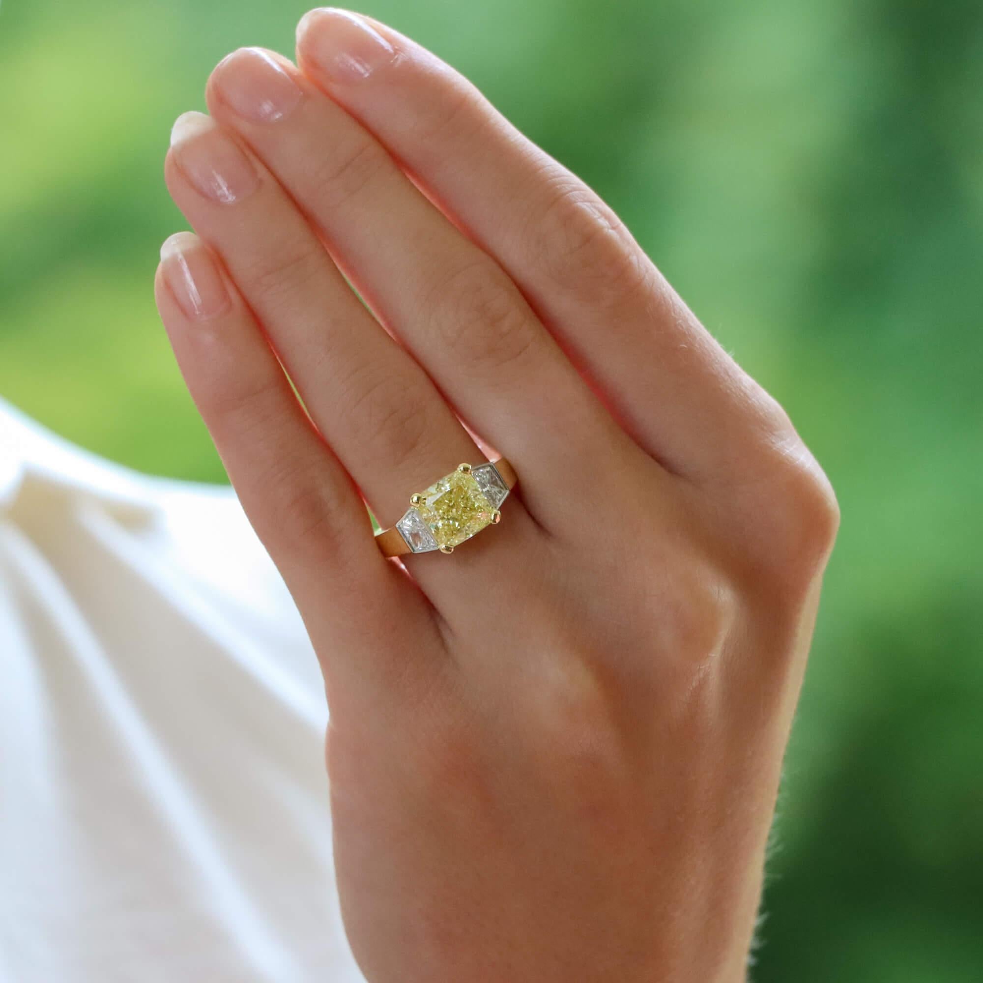 A beautiful GIA certified fancy yellow diamond three stone ring set in 18k yellow and white gold.

The piece is predominantly set with an astounding GIA certified 3.51 carat natural fancy yellow cushion cut diamond which is securely four claw set to