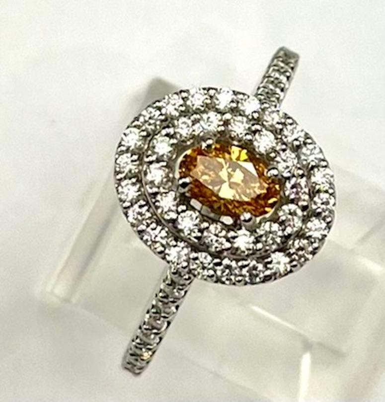 This ring features a rare Vivid Yellow Orange Oval Diamond that is both vibrant and alluring. The double halo serves to enhance both  the size and color of the main stone. The color is deep and transparent. The ring definitely captures attention