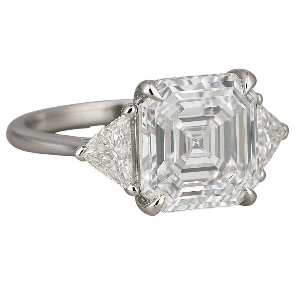 Realizzato in platino lucido, questo sofisticato anello con tre pietre presenta al centro un sorprendente diamante quadrato con taglio a smeraldo da 4 carati, certificato GIA con colore H e purezza VS1. Questa combinazione garantisce una