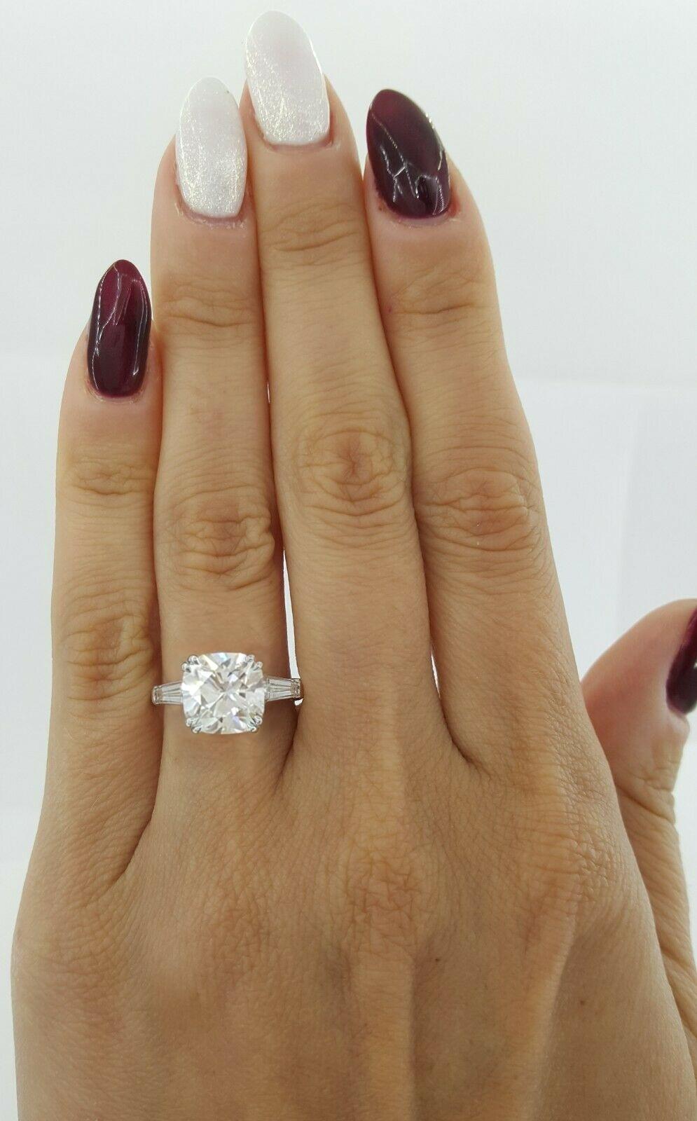This stunning ring features a GIA certified 4.01 carat cushion-cut diamond, elegantly set in a platinum band with tapered baguette side stones. The cushion cut, known for its soft curves and brilliant facets, enhances the diamond’s depth and fire,