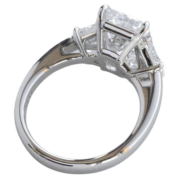 Elevate your sense of luxury with this extraordinary three-stone diamond ring, featuring a magnificent GIA Certified 4.18Carat Emerald Cut Diamond as its focal point. 

This masterpiece boasts a rare E color rating, the highest degree of whiteness