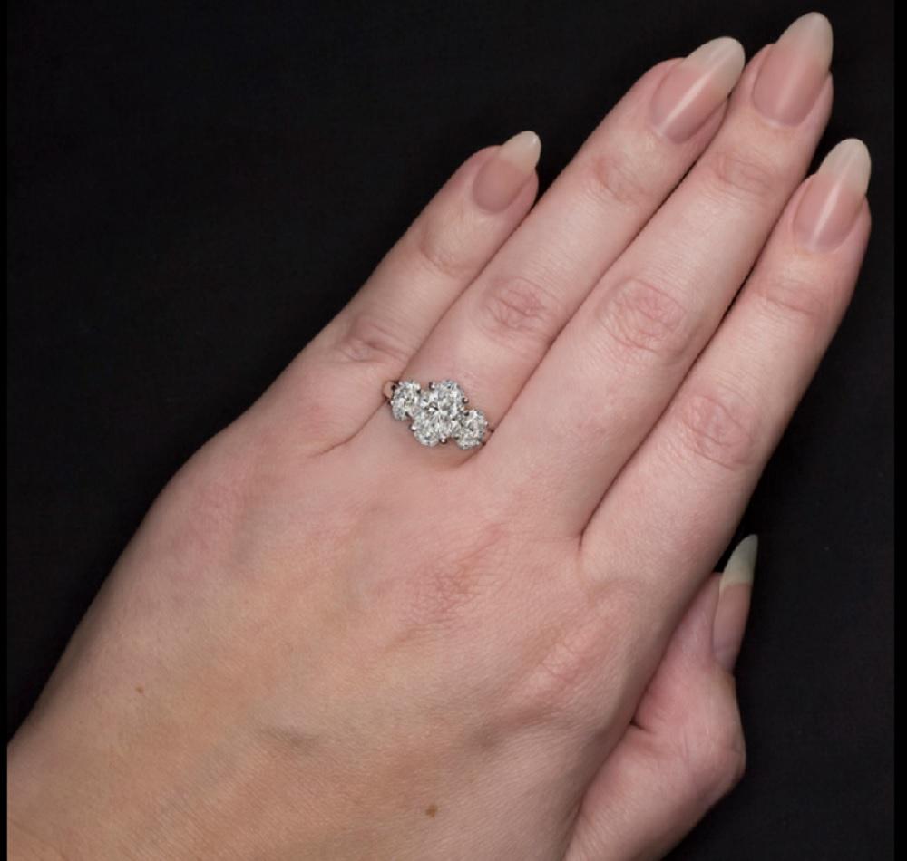 This ring is positively stunning, showcasing a dazzling and impressively large 4 carat GIA certified diamond flanked by two additional certified oval cut diamonds. The glamorously large center cut diamond is 100% eye clean and colorless with