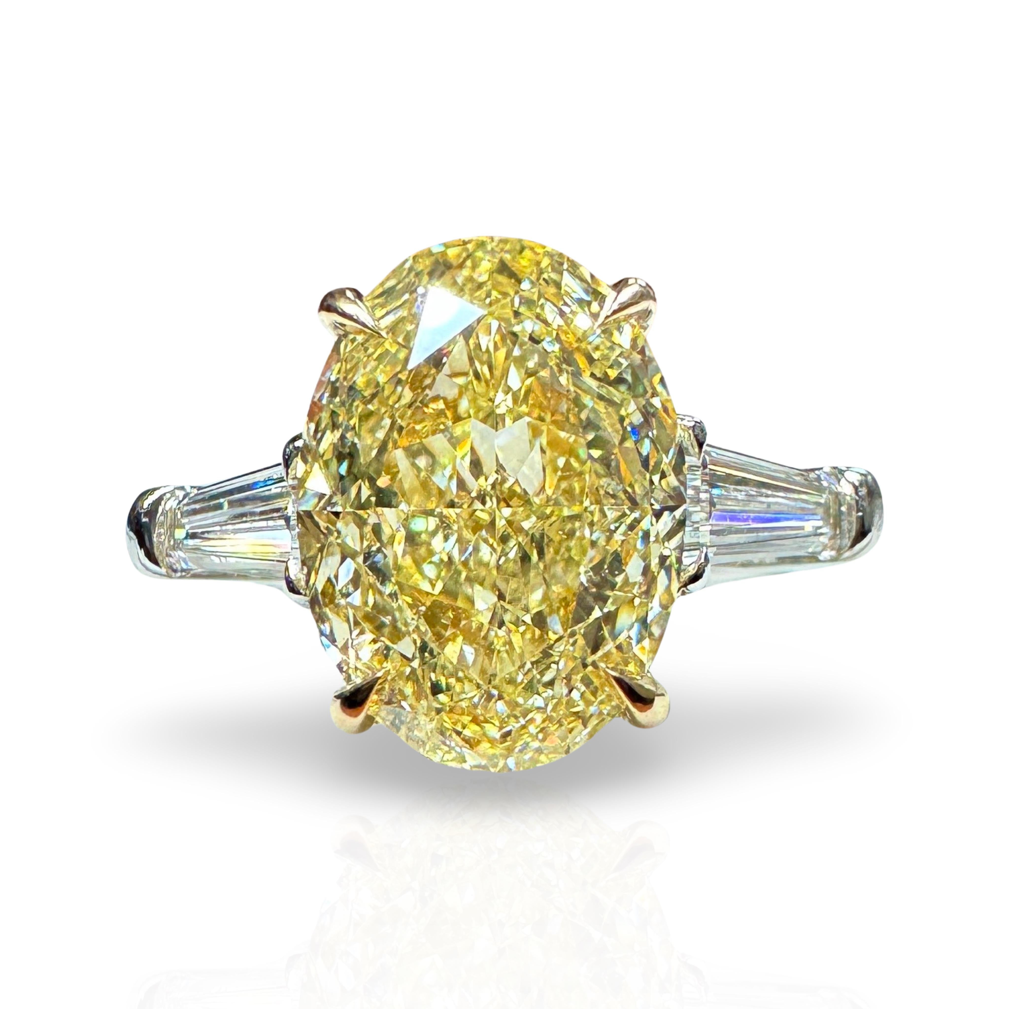 A vibrant GIA Certified Natural Fancy Yellow Oval Cut Yellow Diamond, flanked by two High-Colorless tapered baguette diamonds, also GIA certified. 
The Oval center stone was cut in a way that produces zero 